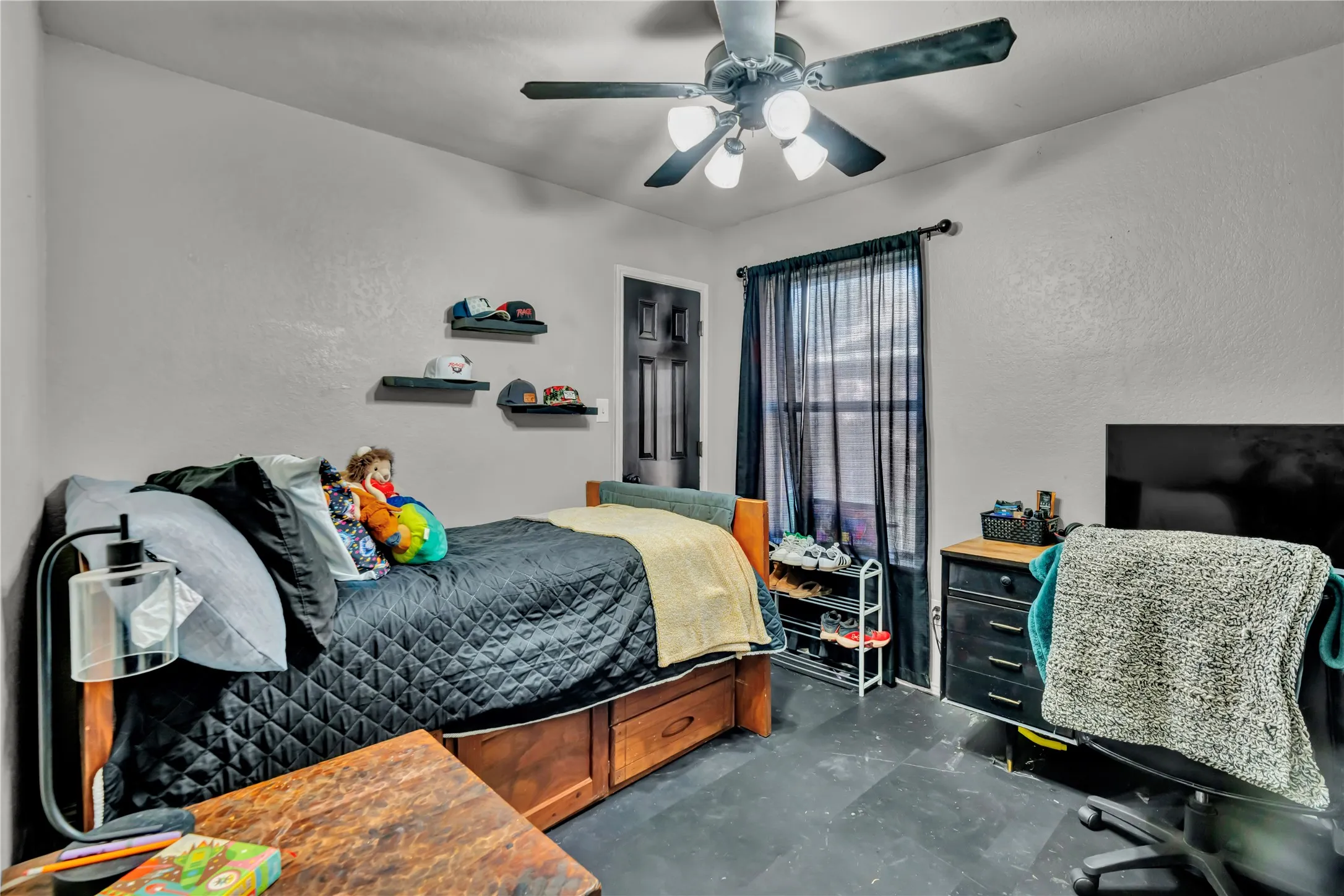 Ceiling fan with integrated lighting, wood-finish flooring, dark-toned window treatments, and a built-in bed frame with storage drawers