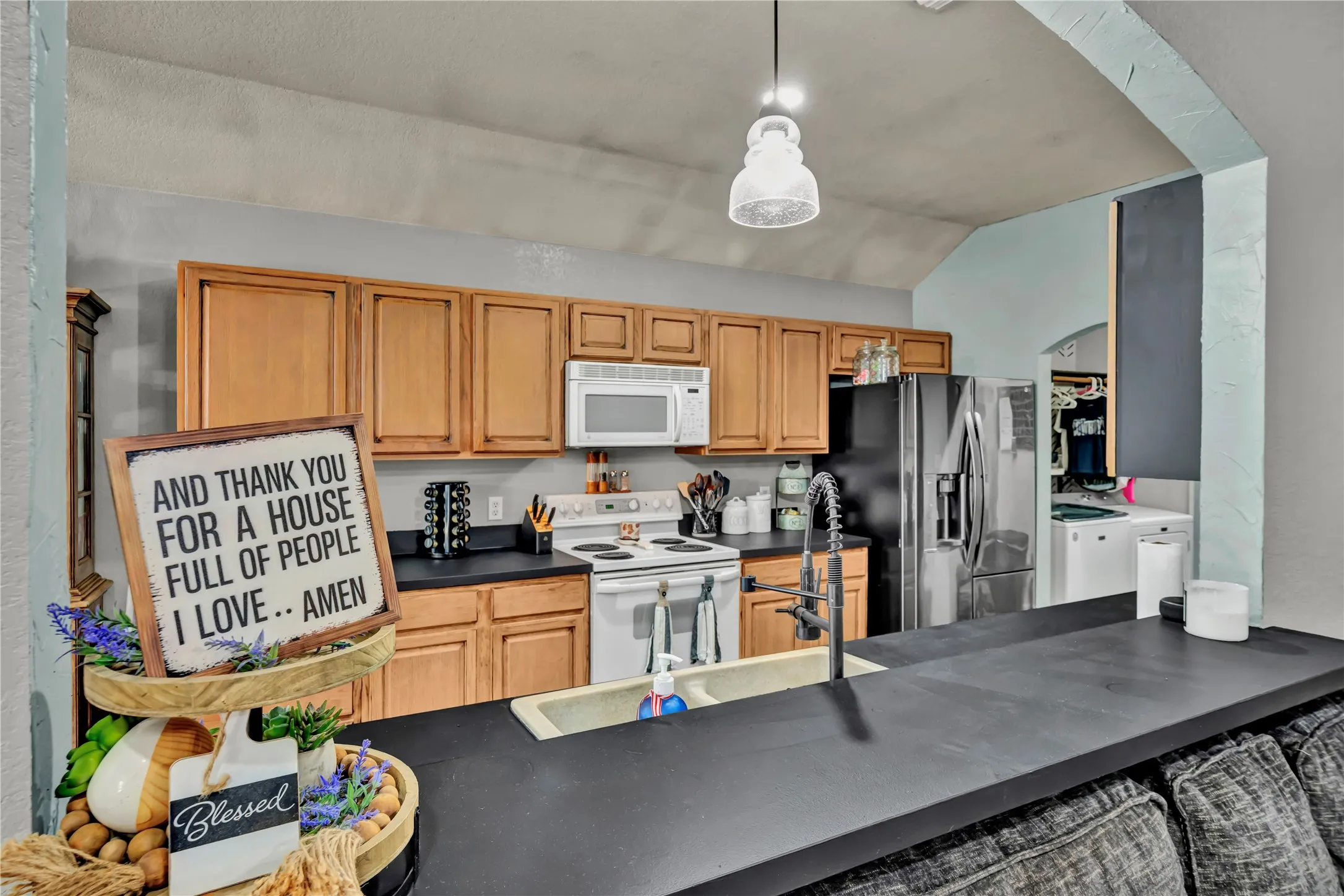 Kitchen featuring wood cabinetry, black countertops, stainless steel refrigerator, and white range