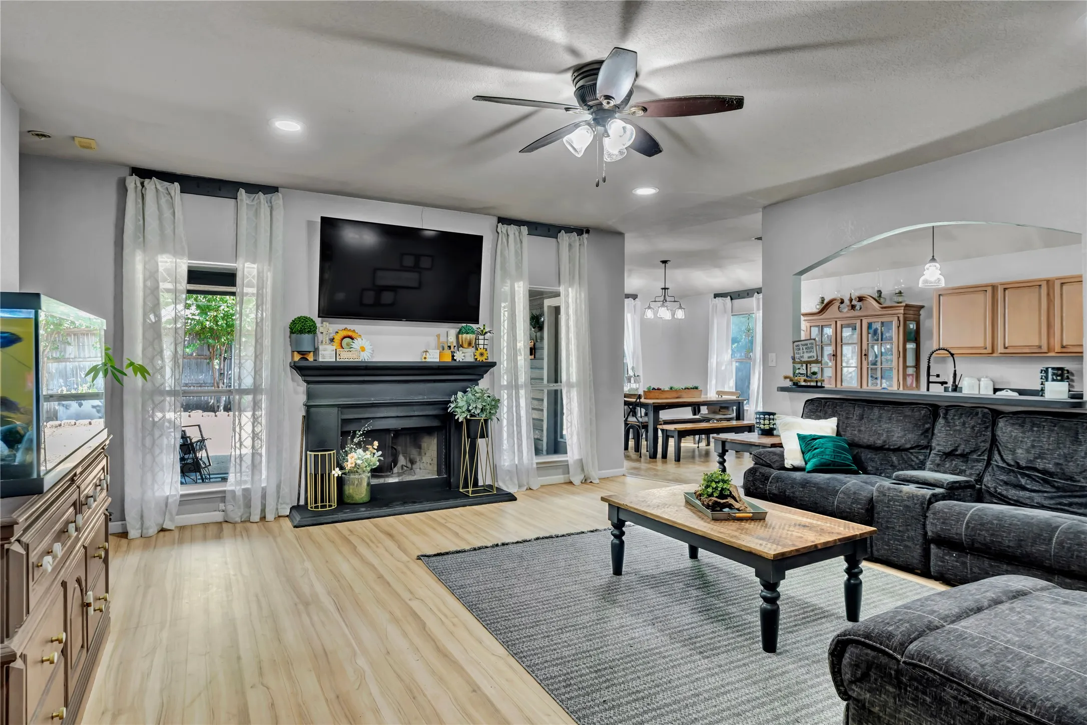 Recessed lighting, wood-finish flooring, ceiling fan with light fixture, built-in fireplace, and an arched entryway to the kitchen