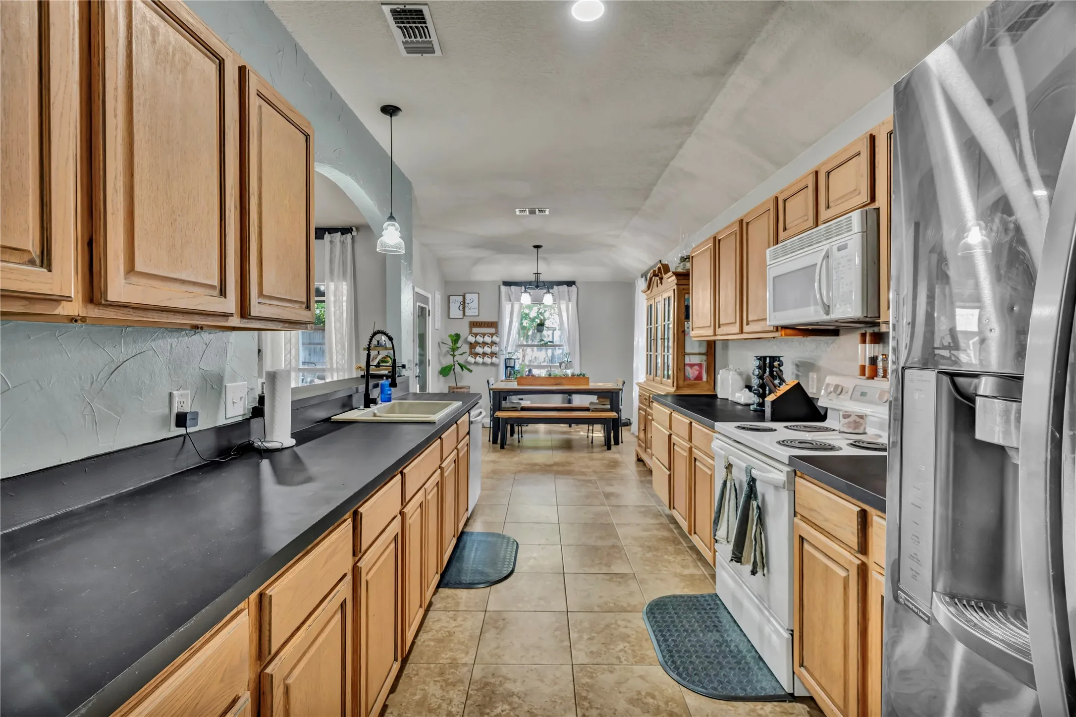 Galley kitchen featuring light wood-finish cabinetry, dark countertops, and tile flooring