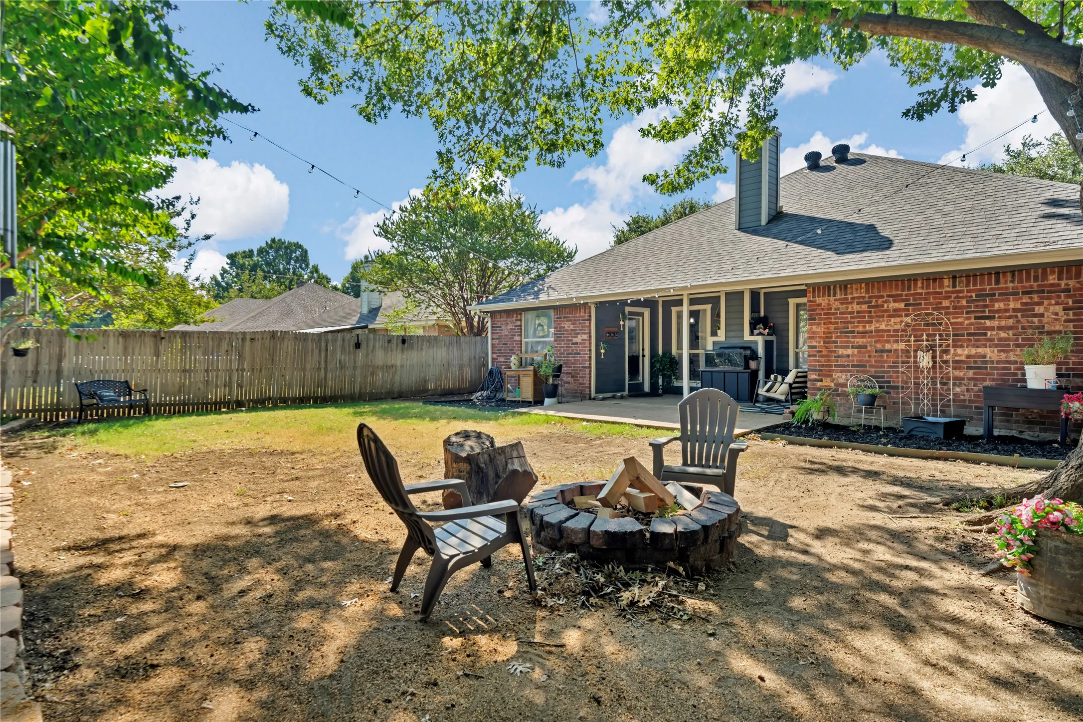Expansive backyard with a fire pit, mature tree, brick exterior, and covered patio