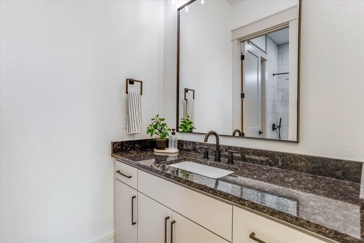 Vanity with dark granite countertop, undermount sink, dark bronze faucet, and rectangular mirror