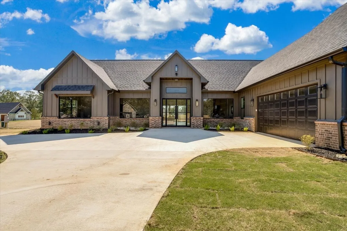 Siding with vertical board and batten details, brick accents, multiple large windows, a prominent entry, and a multi-car garage with paneling