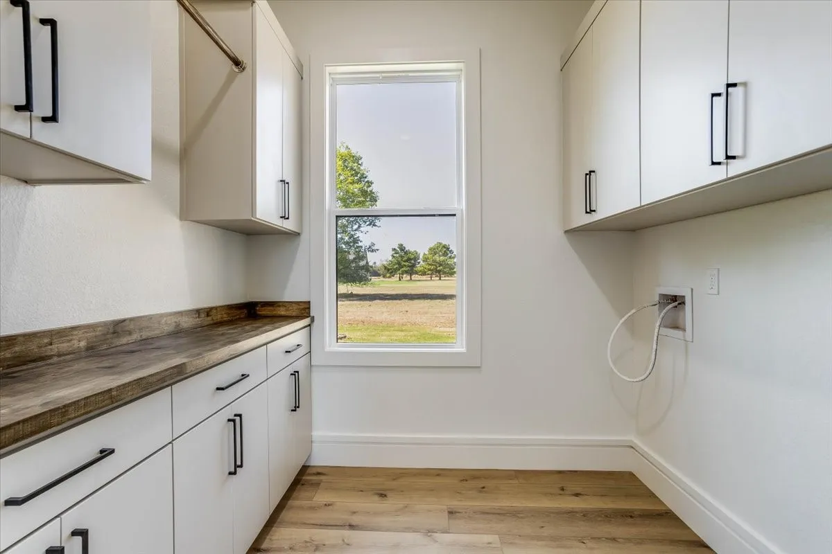 White cabinetry with black hardware, wood-finish countertop, wood-finish flooring, and a single window