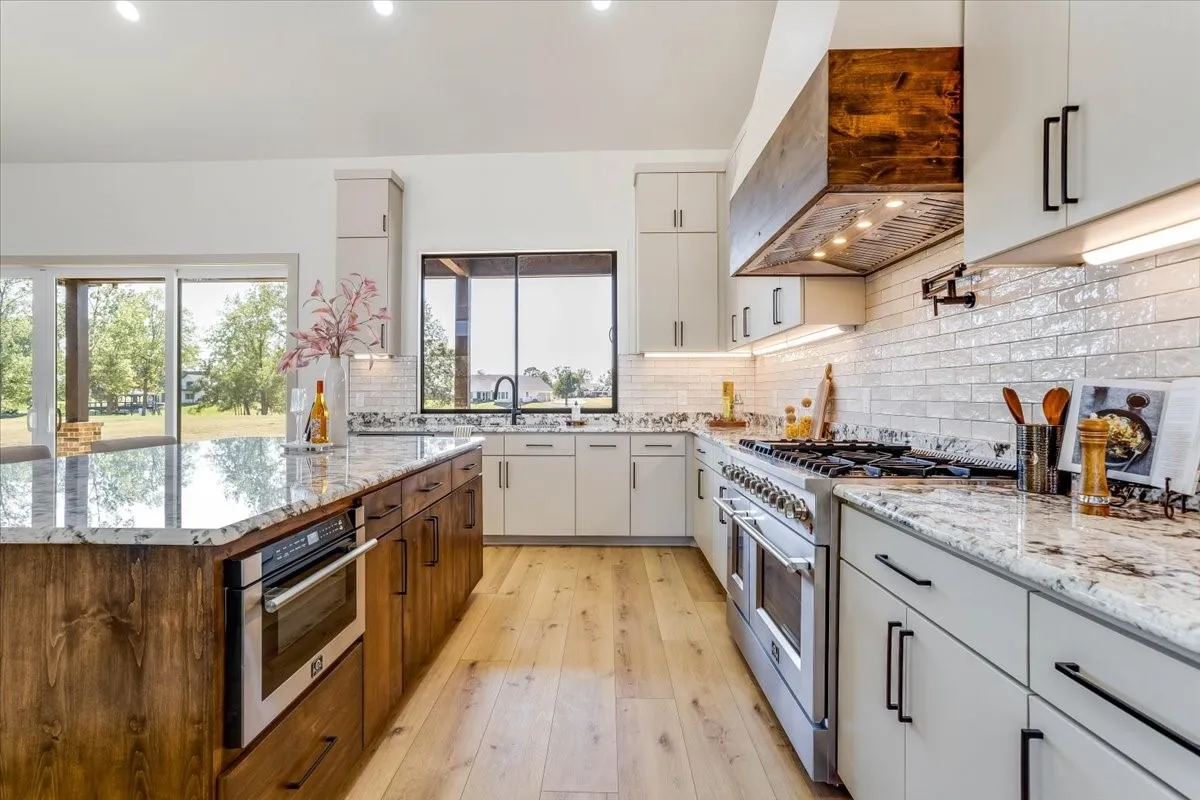 Gourmet kitchen featuring a large central island with an integrated microwave, stainless steel range, custom vent hood, LVP flooring, white subway tile backsplash, and light-toned cabinetry with dark hardware