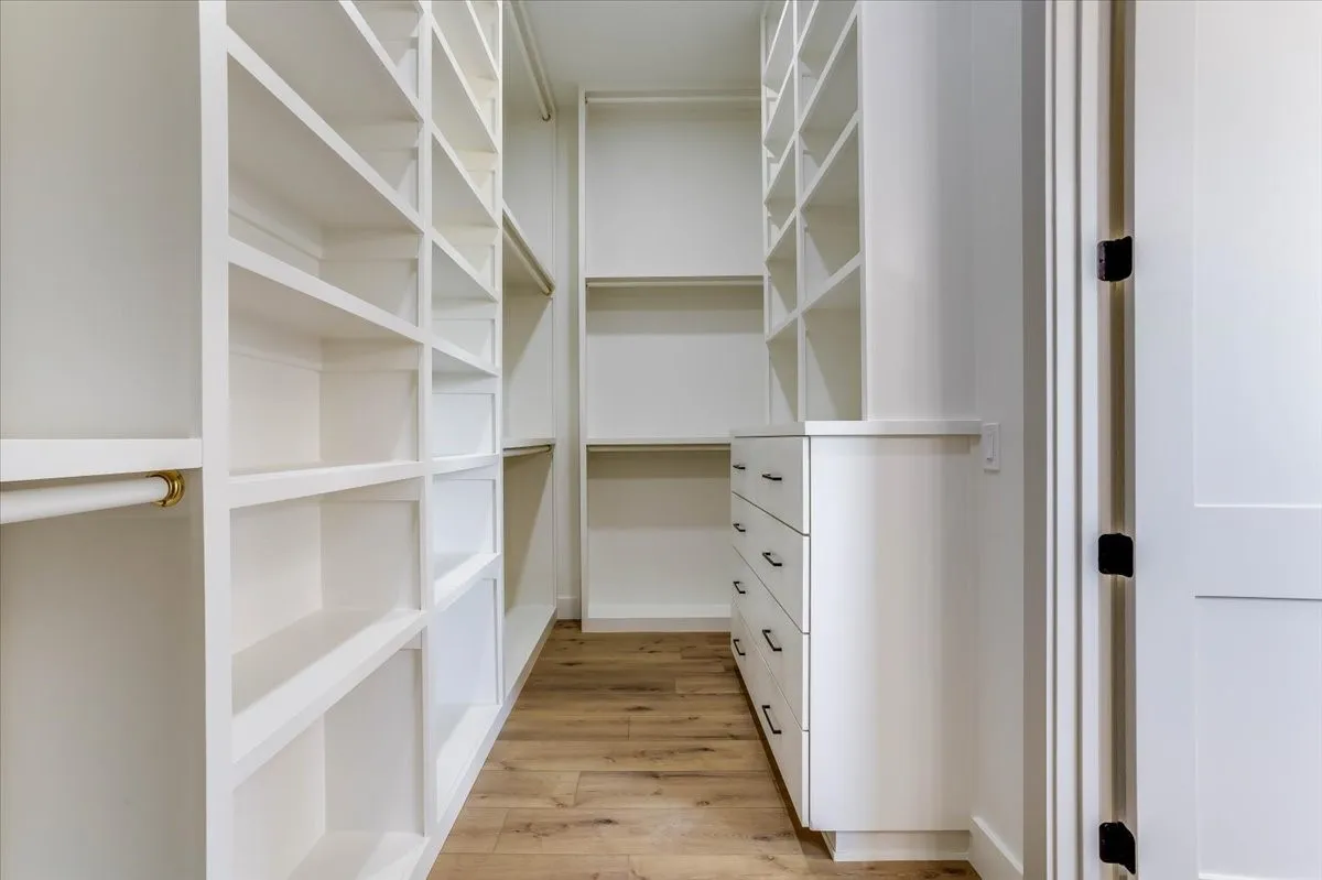Custom built-in shelving, integrated drawers with dark hardware, hanging rod, and wood-finish flooring