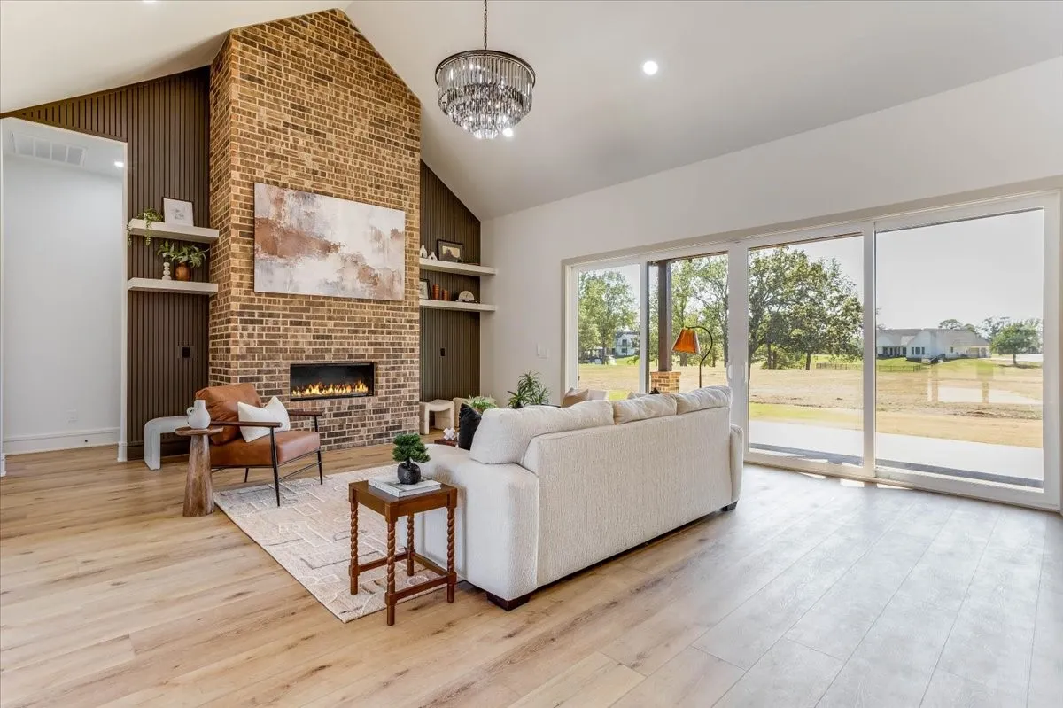 Vaulted ceiling with a contemporary chandelier, brick fireplace with a linear insert, wood-finish flooring, and large sliding glass doors