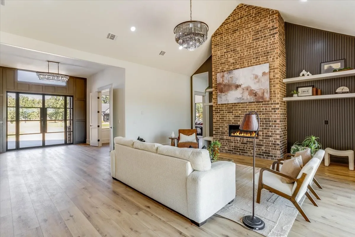 Vast living area featuring wood-finish flooring, a vaulted ceiling, and a brick fireplace