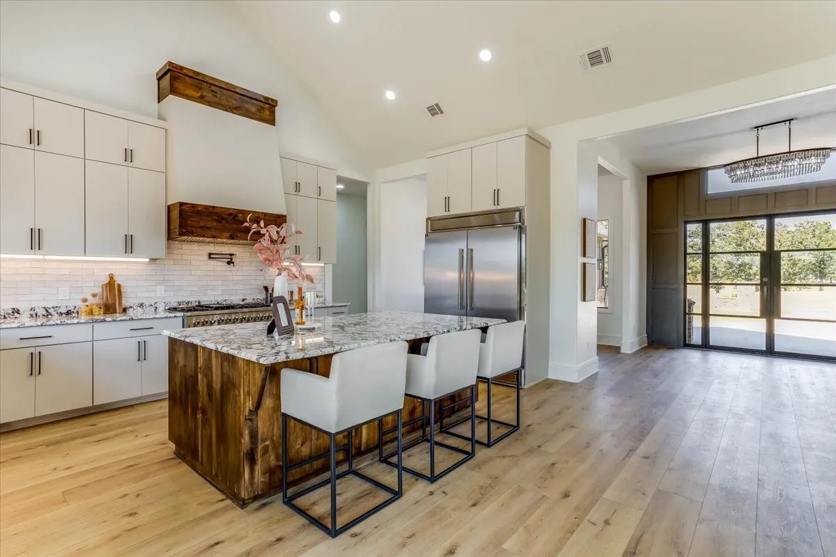 Vaulted ceiling, wood-finish flooring, custom wood-wrapped range hood, kitchen island with granite countertop, and stainless steel appliances