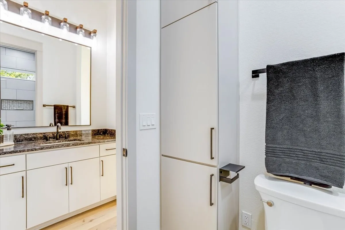 White cabinetry with dark hardware, granite countertop, wood-finish flooring, and built-in storage