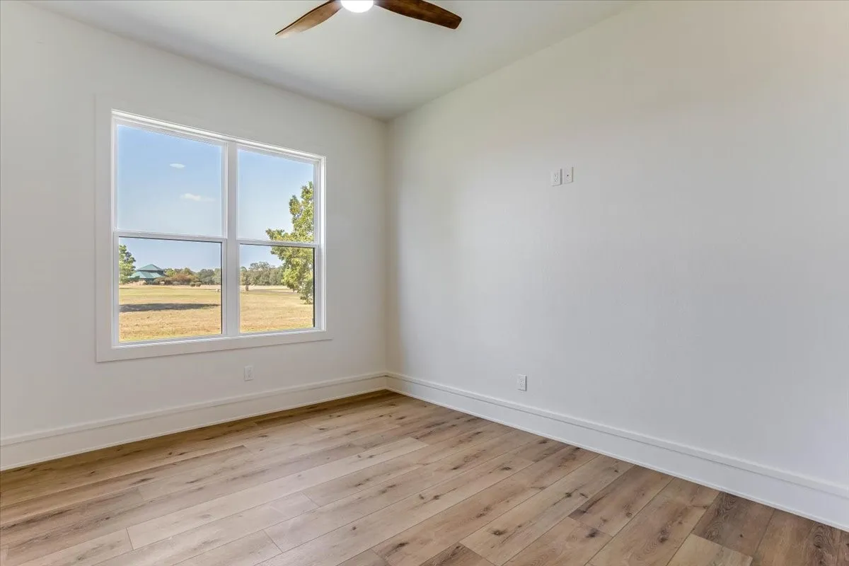 Expansive room featuring wood-finish flooring, a large multi-pane window, and a ceiling fan
