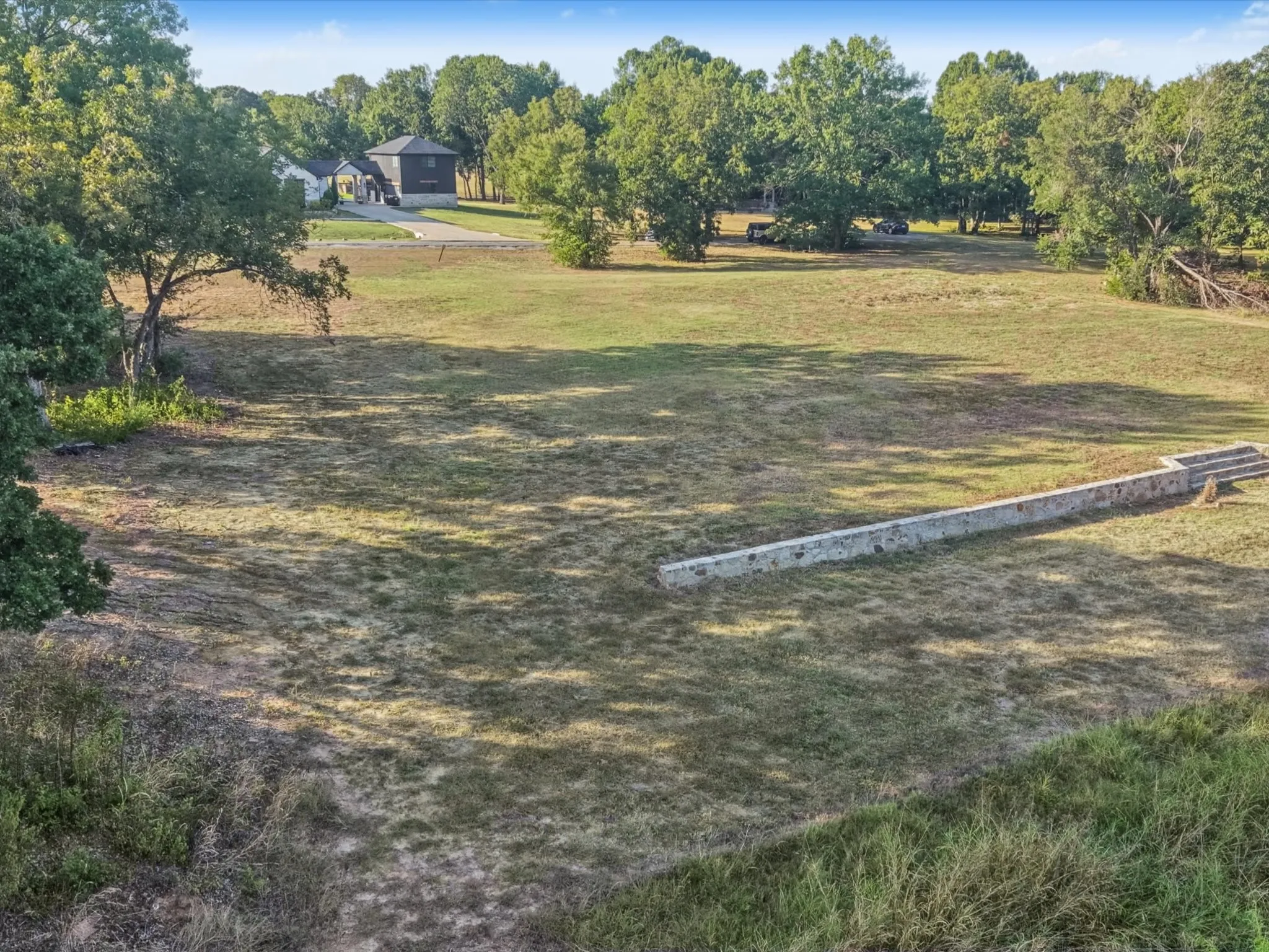 Expansive land parcel featuring a stone retaining wall and a treed perimeter