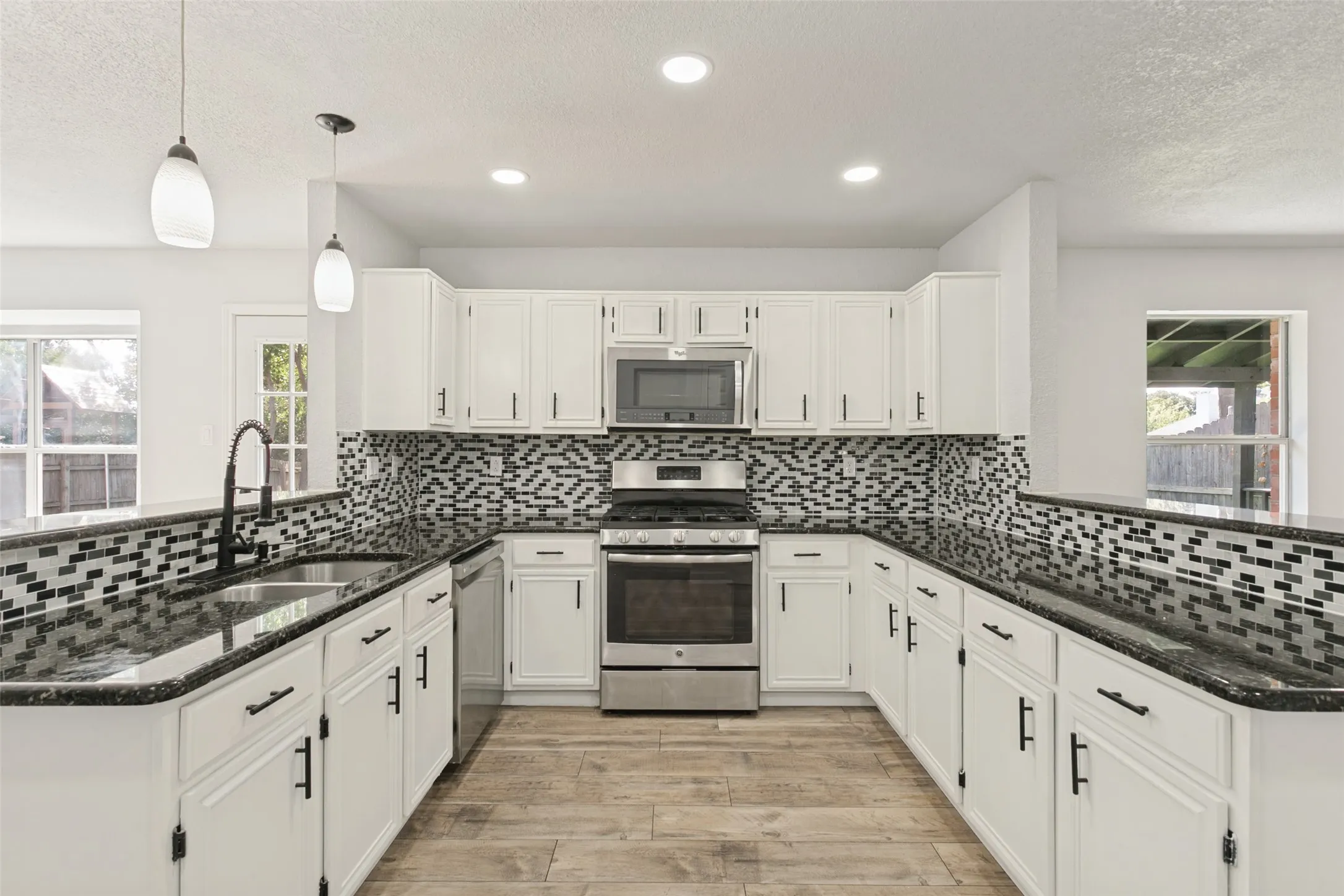 U-shaped kitchen featuring white cabinetry, dark countertops, a mosaic tile backsplash, wood-finish flooring, and stainless steel appliances