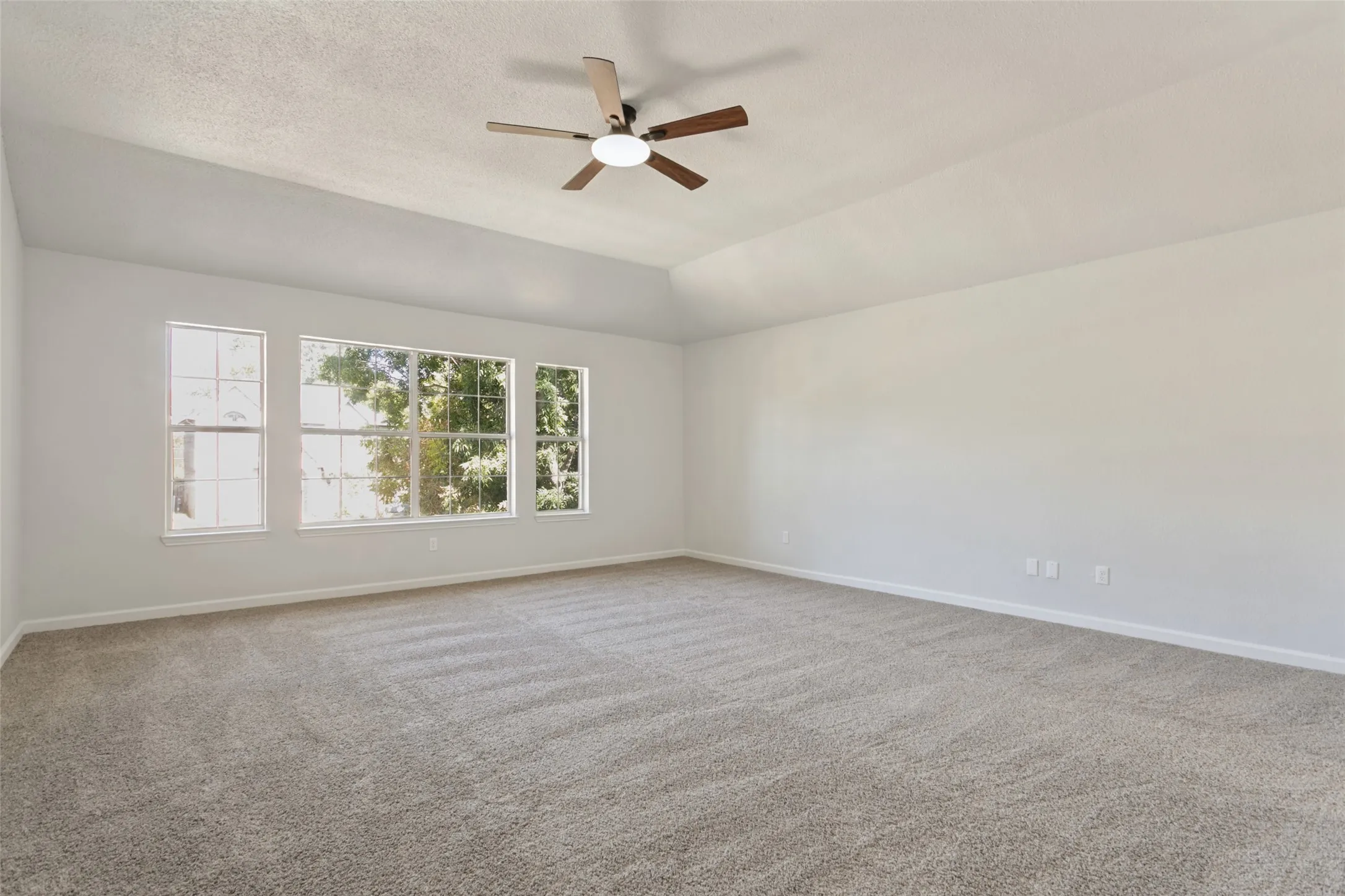 Vaulted ceiling, three large windows, ceiling fan with integrated lighting, and carpeted flooring