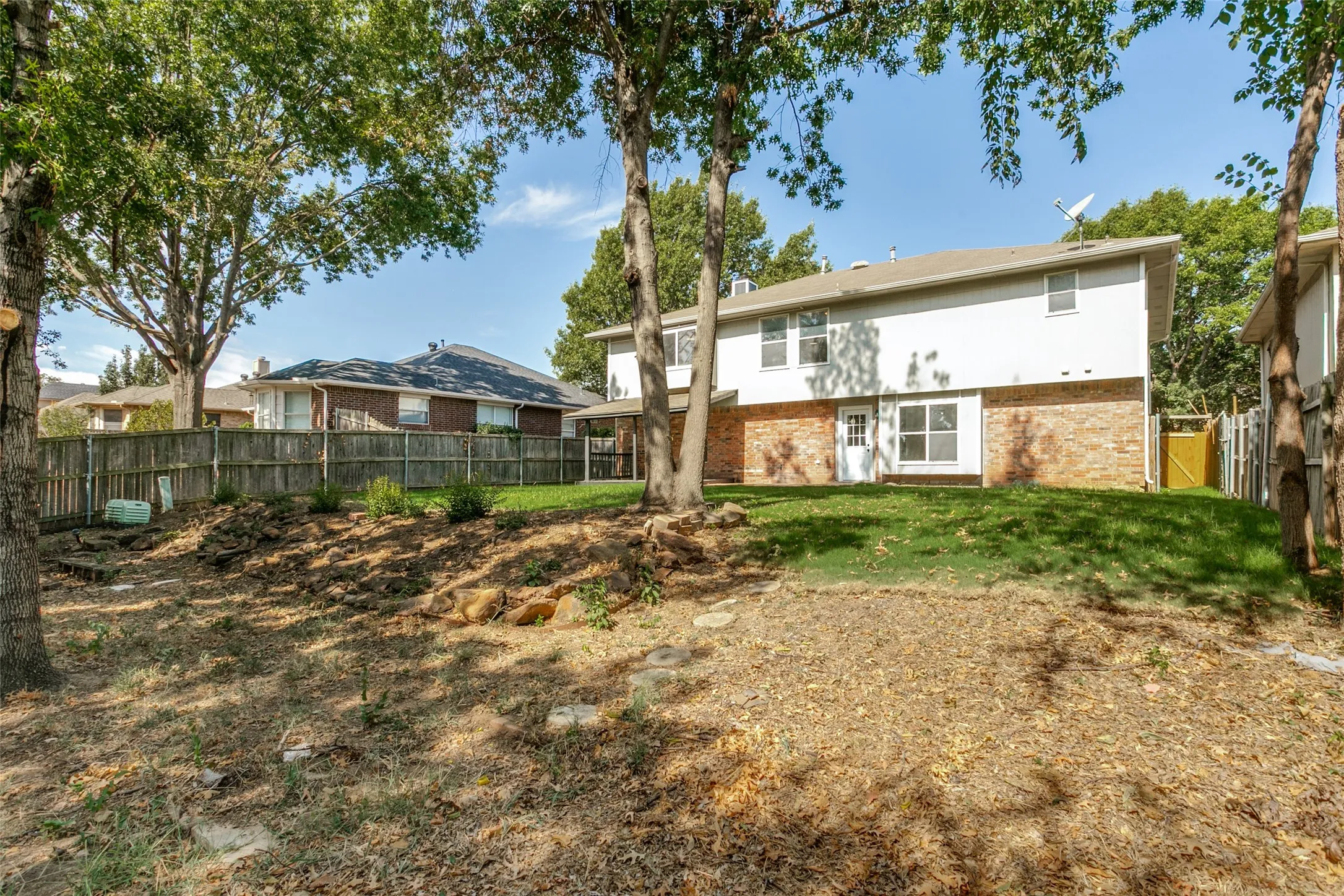Expansive backyard featuring a manicured lawn, partial wood privacy fencing, and mature trees