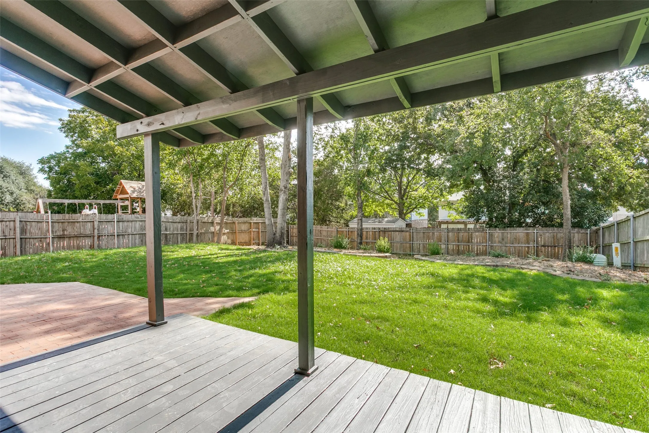 Expansive outdoor living area featuring a covered deck, separate patio, and a fenced yard with mature trees