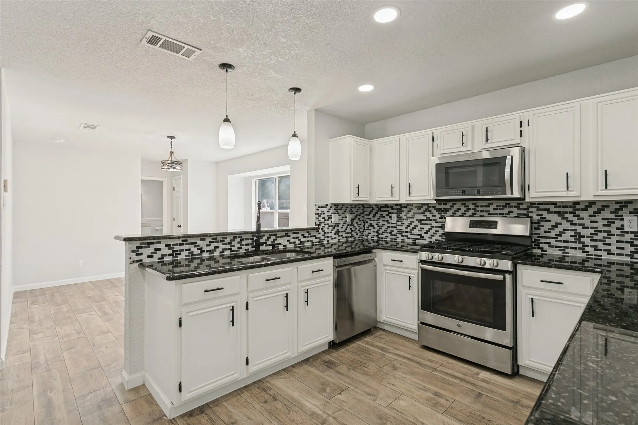 Kitchen featuring white cabinetry, dark countertops, stainless steel appliances, a mosaic tile backsplash, and wood-finish flooring
