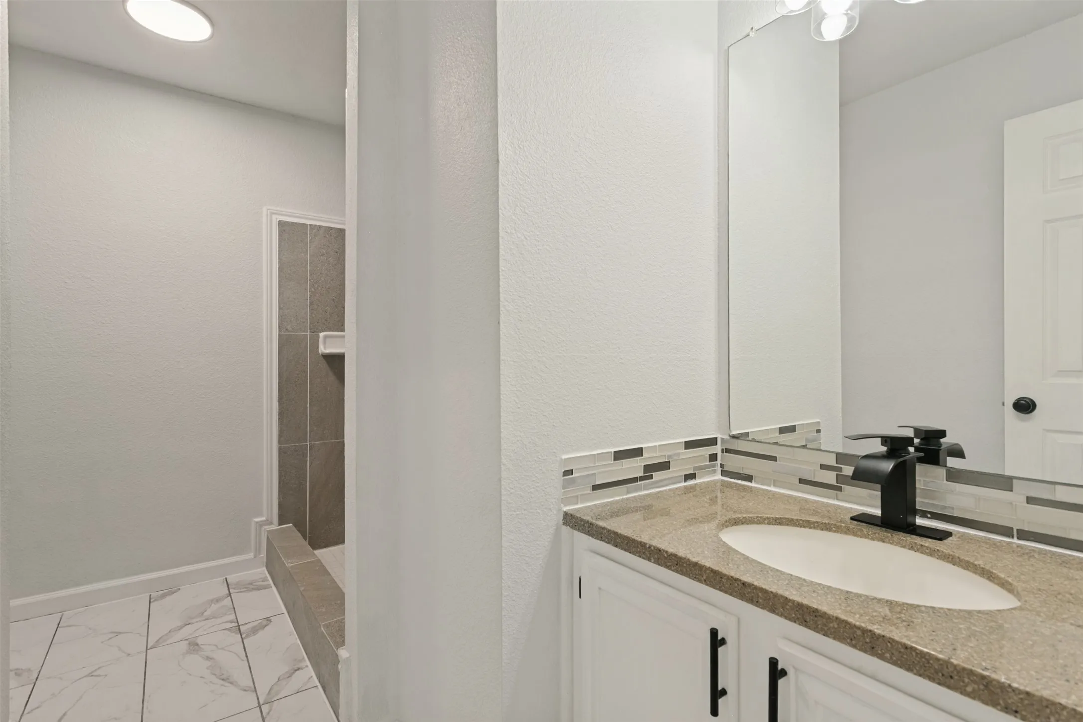 Vanity with an oval undermount sink, dark countertop, and a mosaic tile backsplash