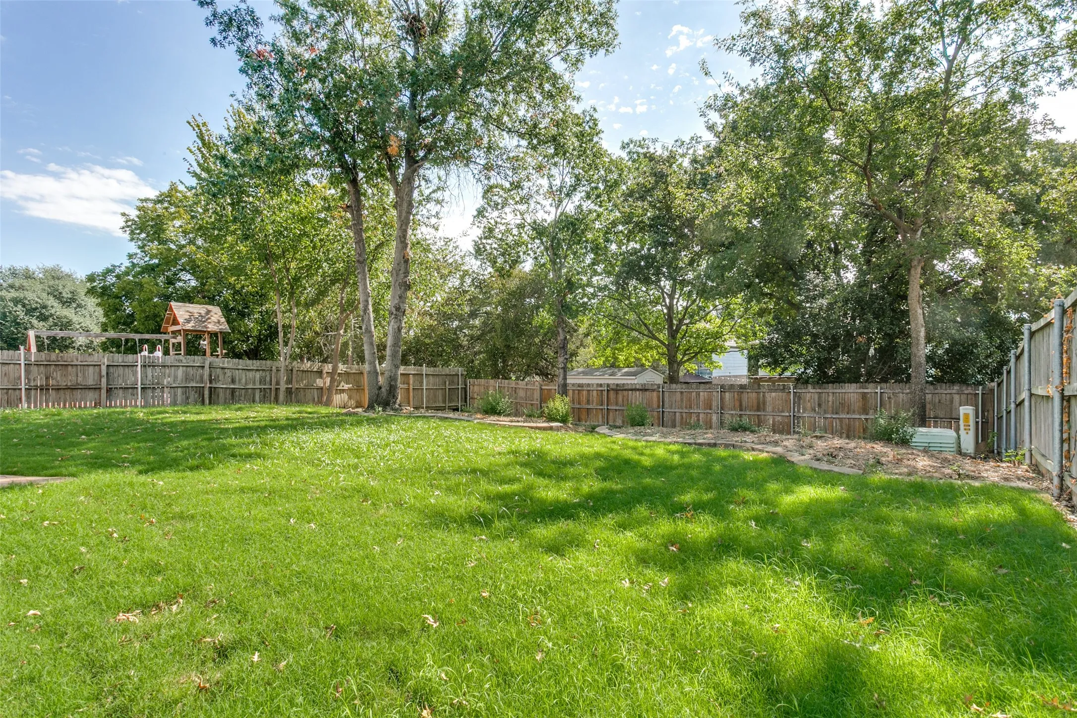 Spacious backyard featuring a lush lawn, mature trees, and privacy fencing
