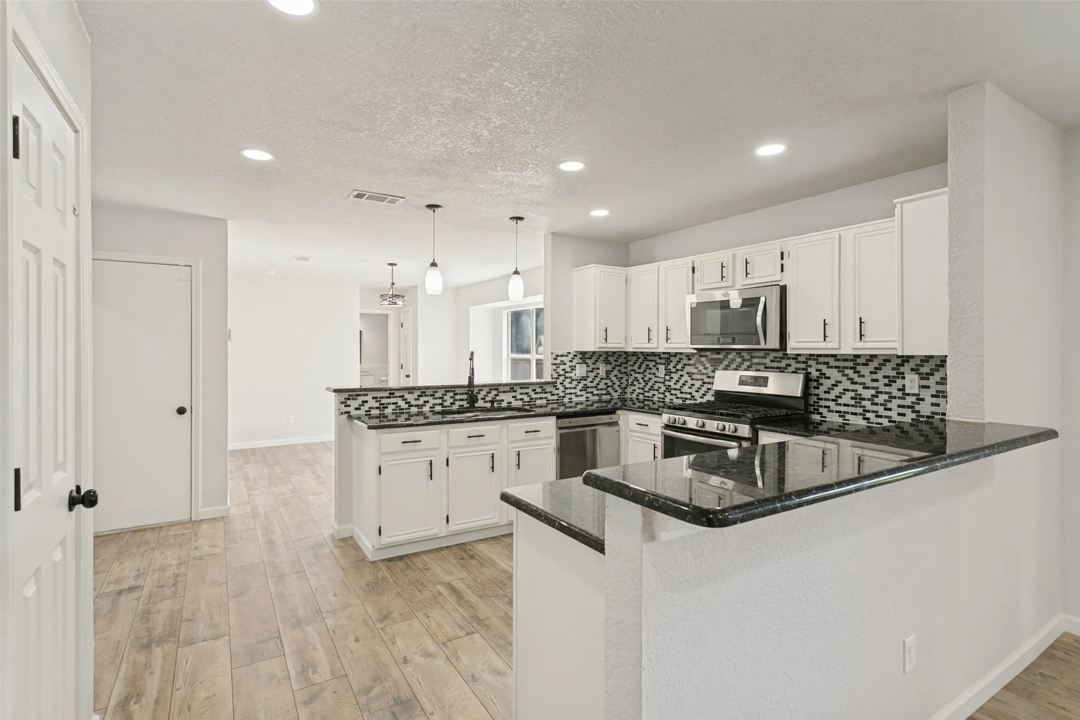 Kitchen featuring white cabinetry, dark countertops, patterned tile backsplash, stainless steel appliances, and wood-finish flooring