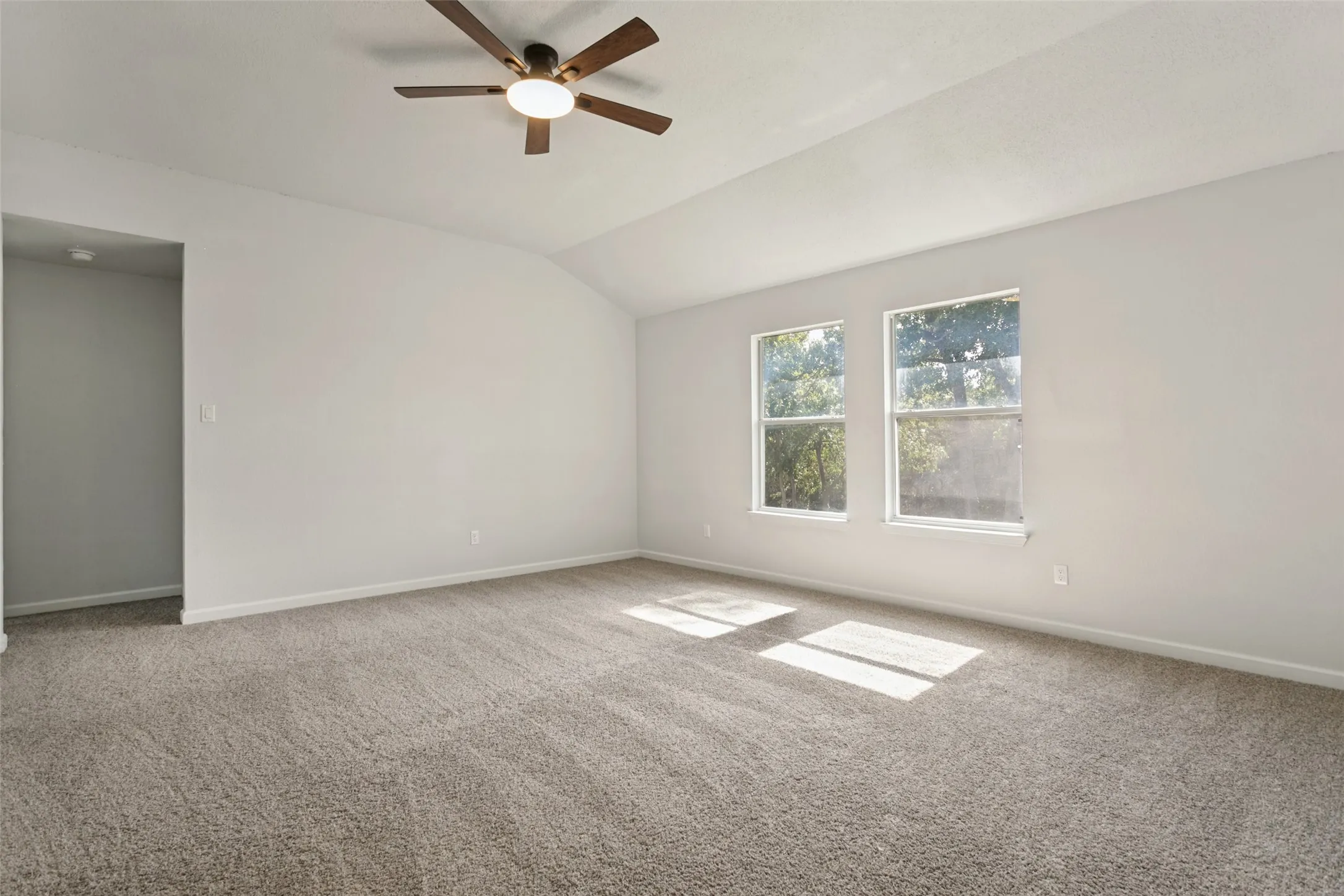 Vaulted ceiling, two windows, ceiling fan with integrated lighting, wall-to-wall carpeting