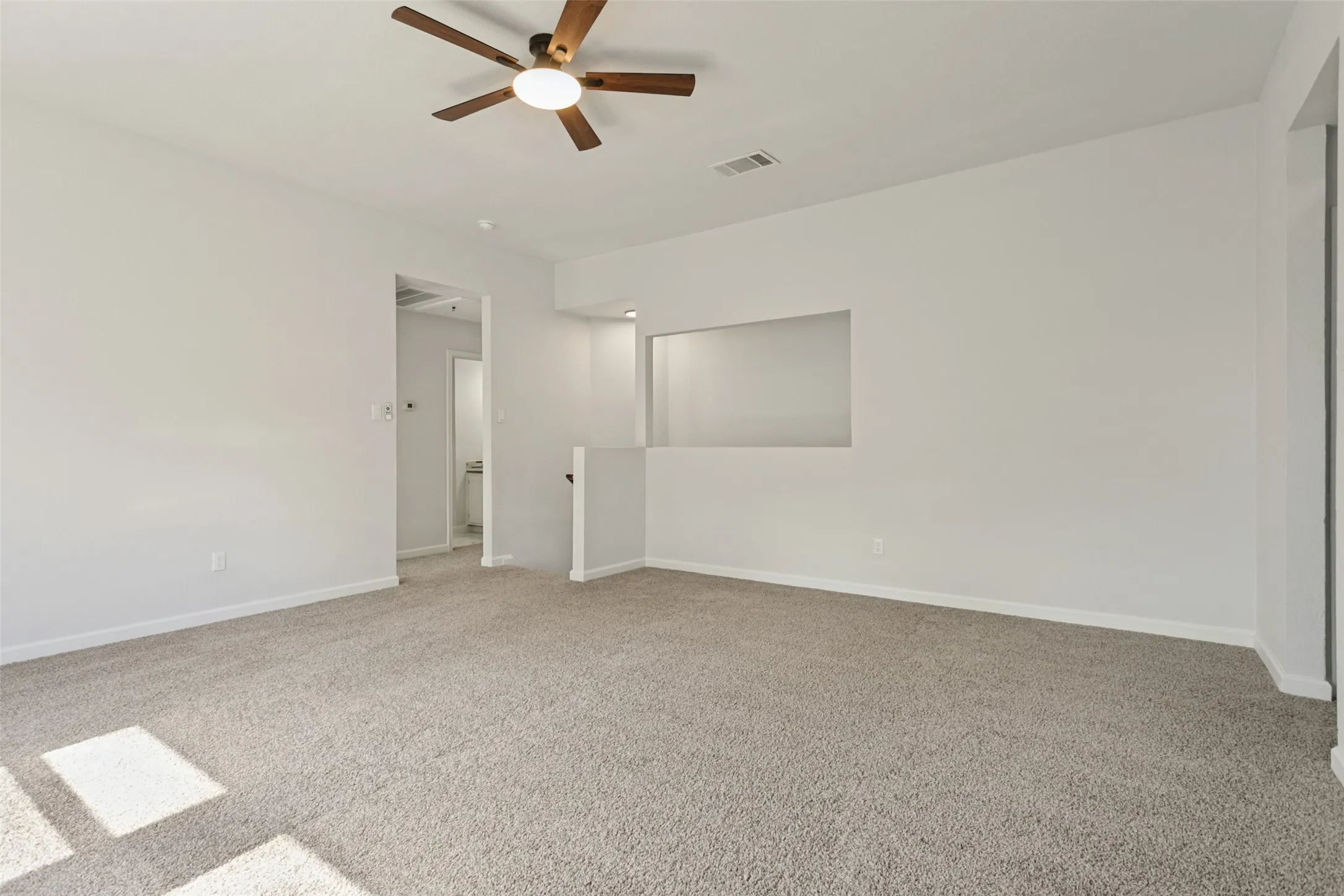 Neutral-toned carpeting throughout with a ceiling fan light fixture and recessed wall niche