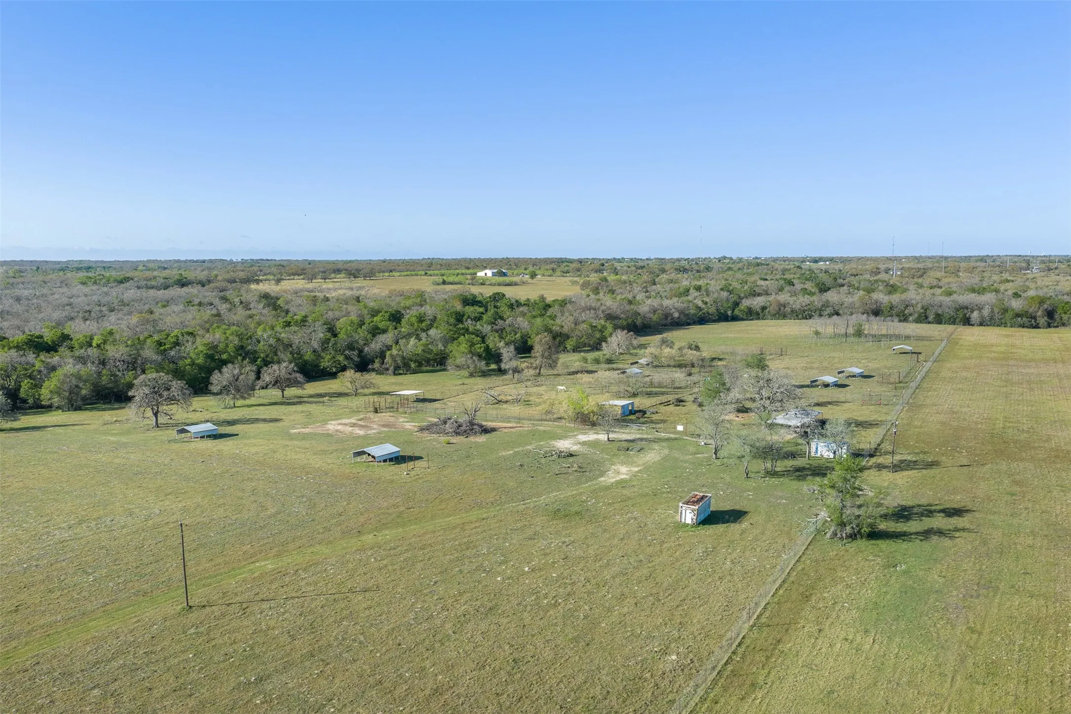 Expansive open fields with scattered trees, multiple outbuildings, and perimeter fencing