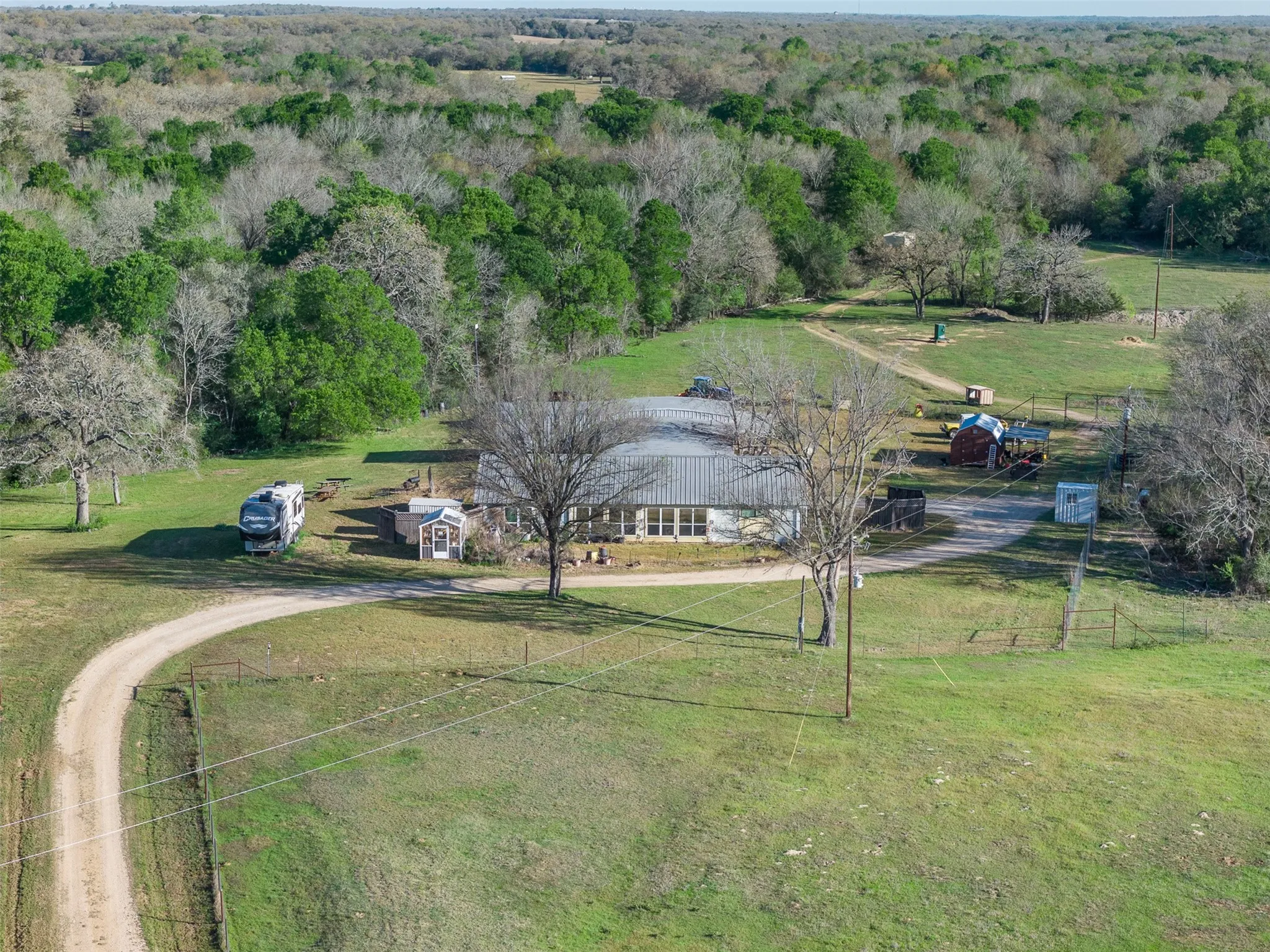 Expansive property featuring a single-story residence with a metal roof, surrounded by mature trees and natural landscaping