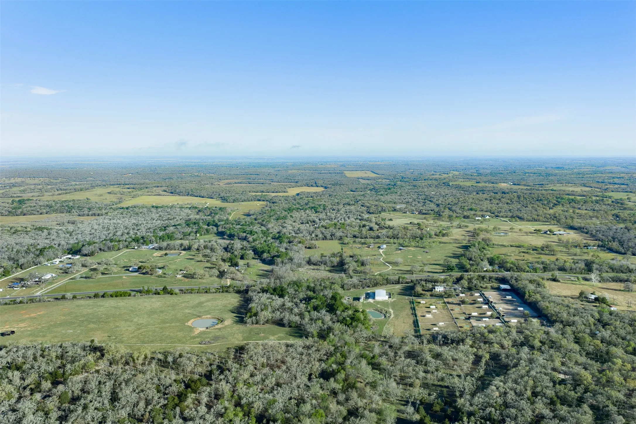 Expansive acreage featuring multiple structures, open fields, forested areas, and a pond