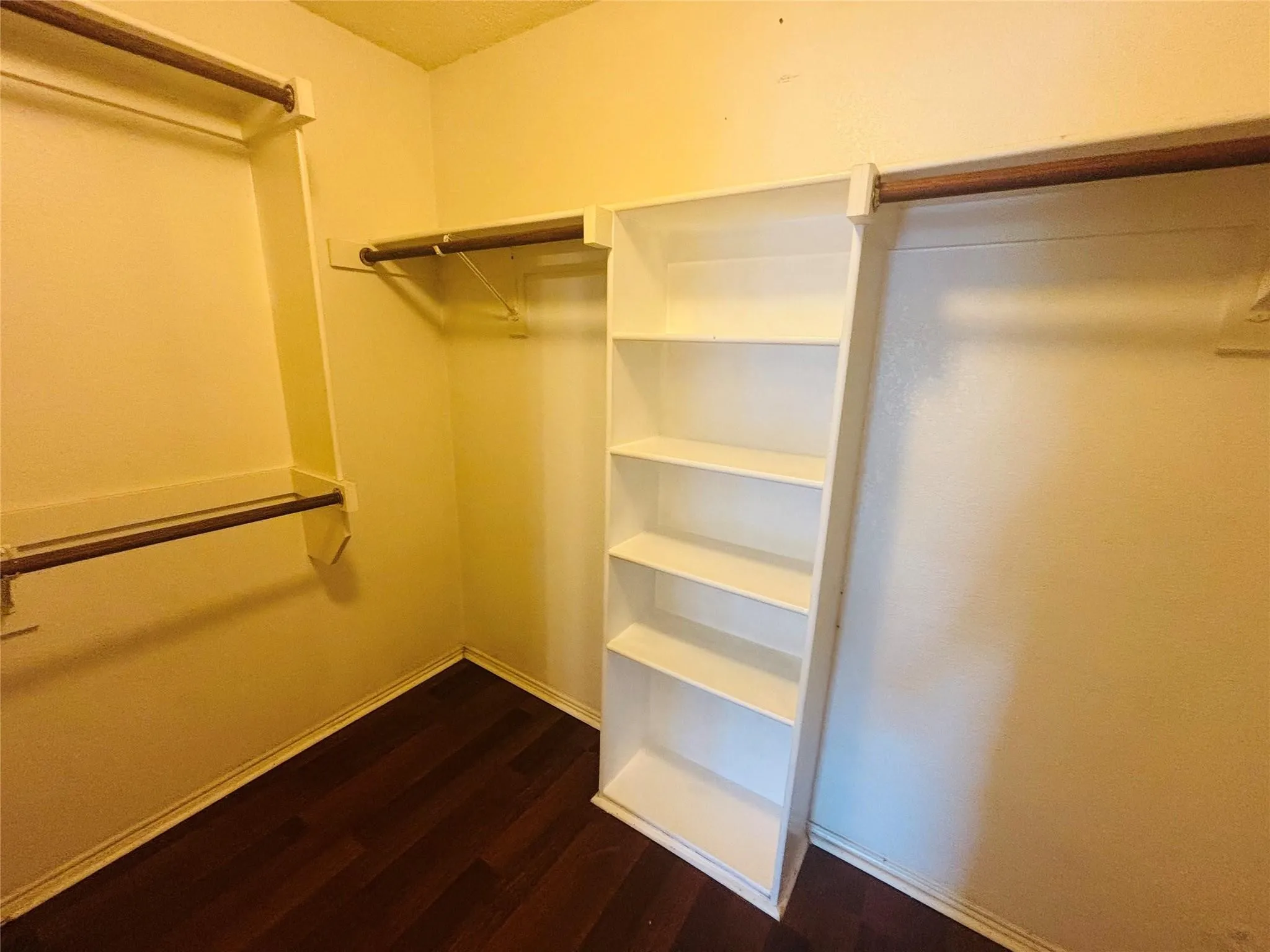 Organized closet space featuring dark wood-finish flooring, multiple hanging rods, and integrated shelving units