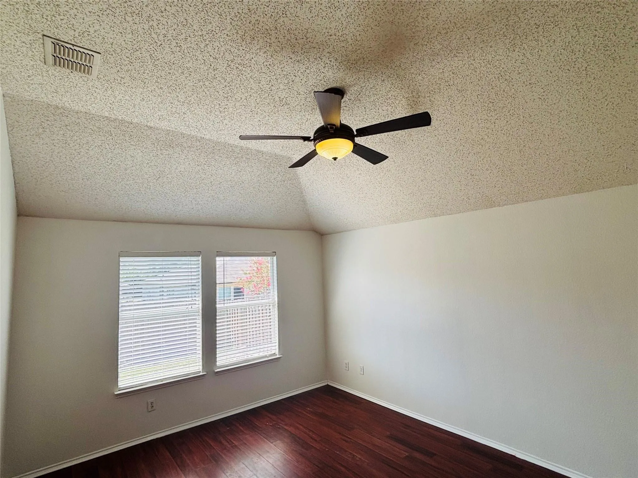 Sloped ceiling with recessed lighting, ceiling fan with integrated light, two windows with blinds, wood-finish flooring, and white walls
