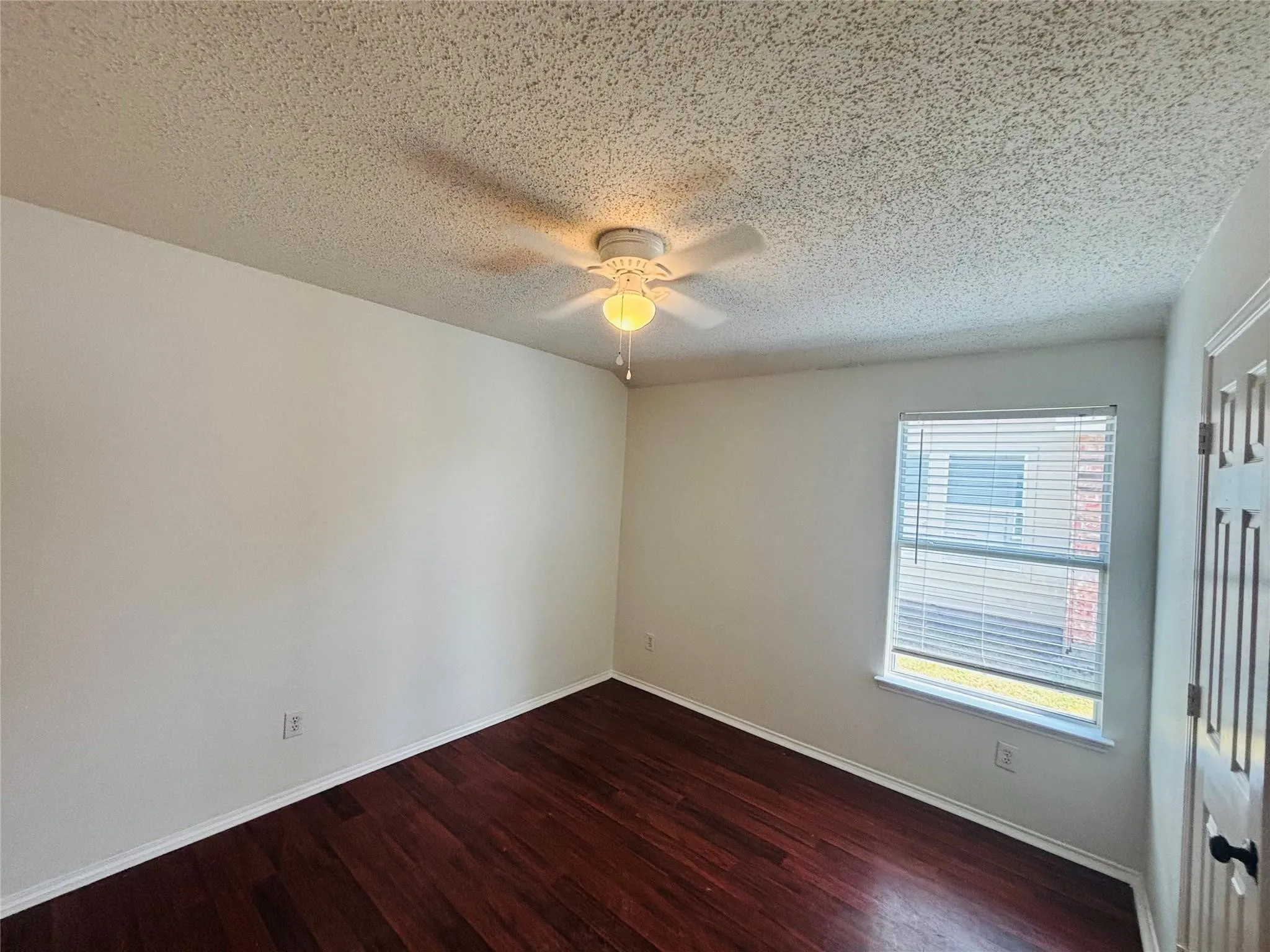Wood-finish flooring, ceiling fan with light fixture, window with blinds, and paneled door with black hardware