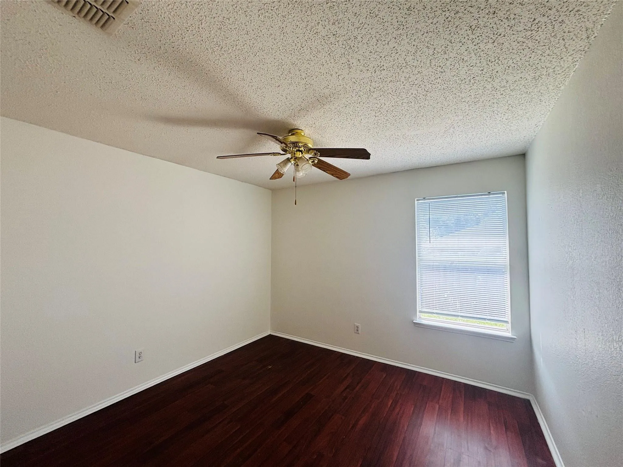 Dark wood-finish flooring, a ceiling fan with light fixture, and a window with blinds