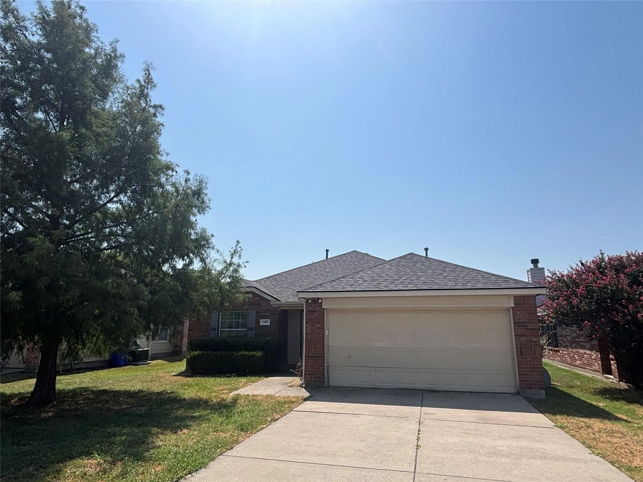 Brick facade with an attached two-car garage, concrete driveway, and mature landscaping