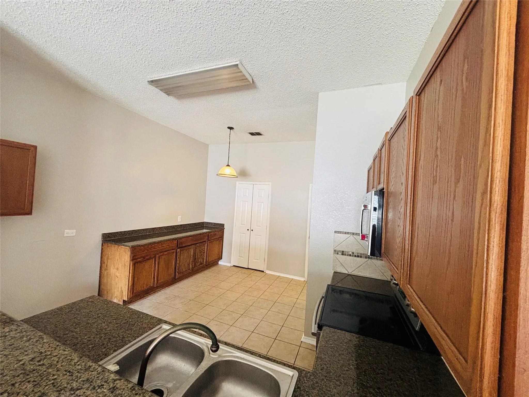 Kitchen featuring wood cabinetry, granite-finish countertops, stainless steel sink, tiled flooring, and a built-in microwave