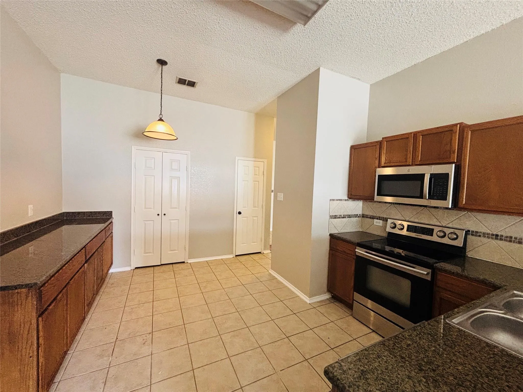 Kitchen featuring ceramic tile flooring, wood cabinetry, stone countertops, stainless steel appliances, and a mosaic tile backsplash