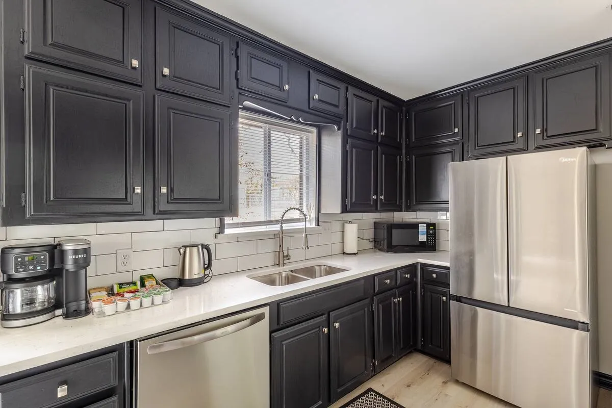Black shaker-style cabinetry with silver hardware, white countertops, white subway tile backsplash, stainless steel appliances, and wood-finish flooring
