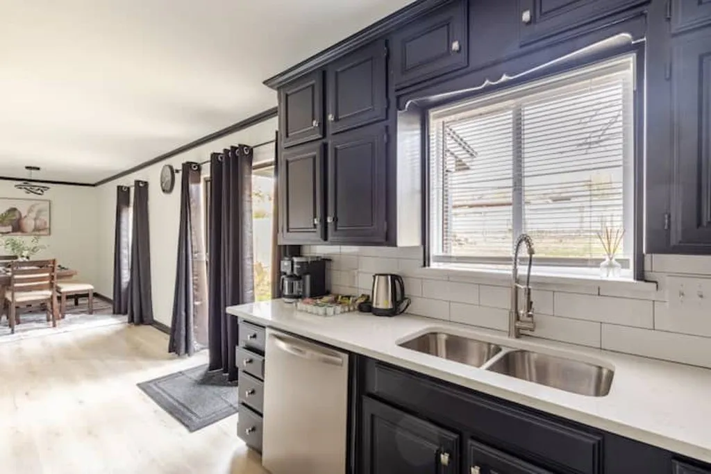 Kitchen featuring dark cabinetry, light-toned countertops, a stainless steel dishwasher, and a dual-basin sink with a gooseneck faucet