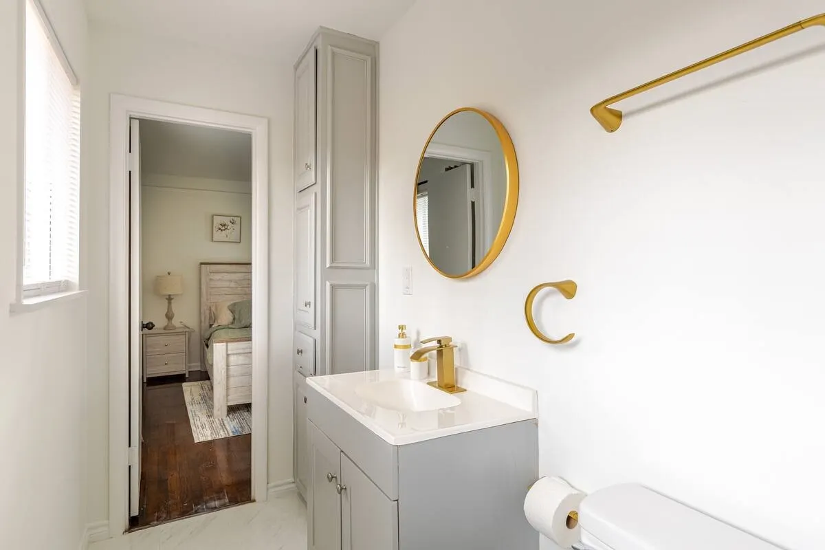 Vanity with integrated sink and gold-finish faucet, framed circular mirror, and built-in vertical cabinetry