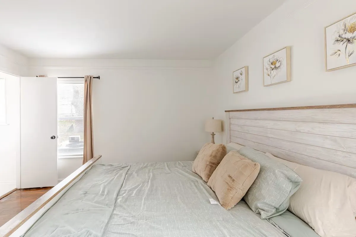 White walls with crown molding, wood-finish flooring, and a window with a curtain rod