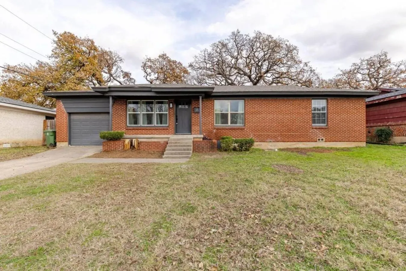 Brick exterior with a dark gray garage door, covered porch, and concrete steps