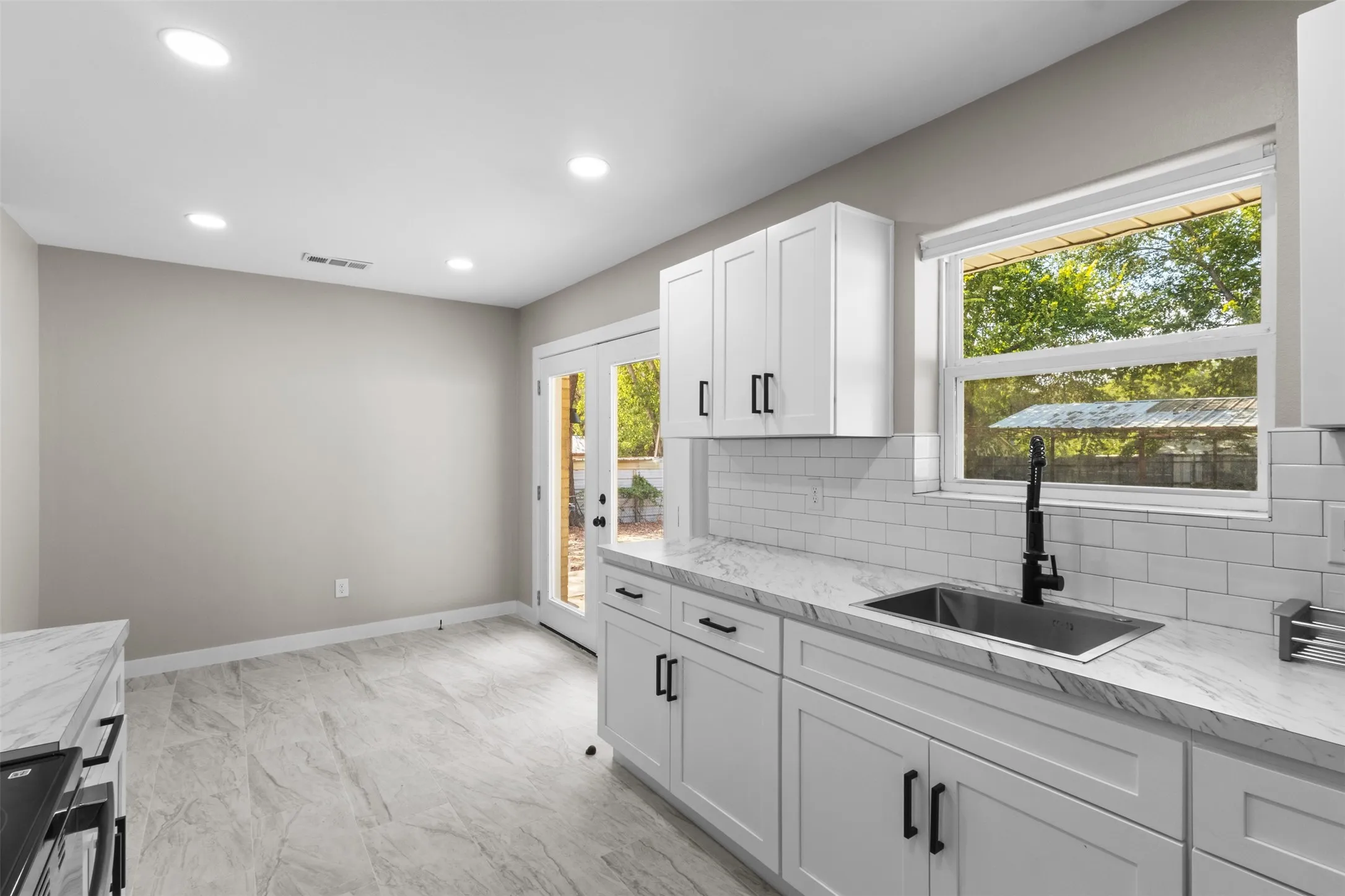 Contemporary kitchen featuring white cabinetry, stone-finish countertops, stainless steel sink with matte black faucet, subway tile backsplash, and recessed lighting