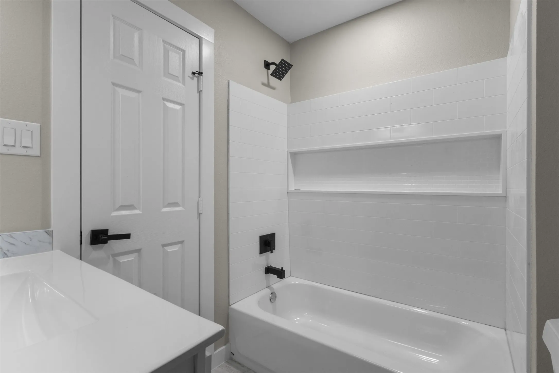 Bathroom featuring a white bathtub, subway tile surround with integrated shelving, matte black fixtures, and a white vanity with an integrated sink