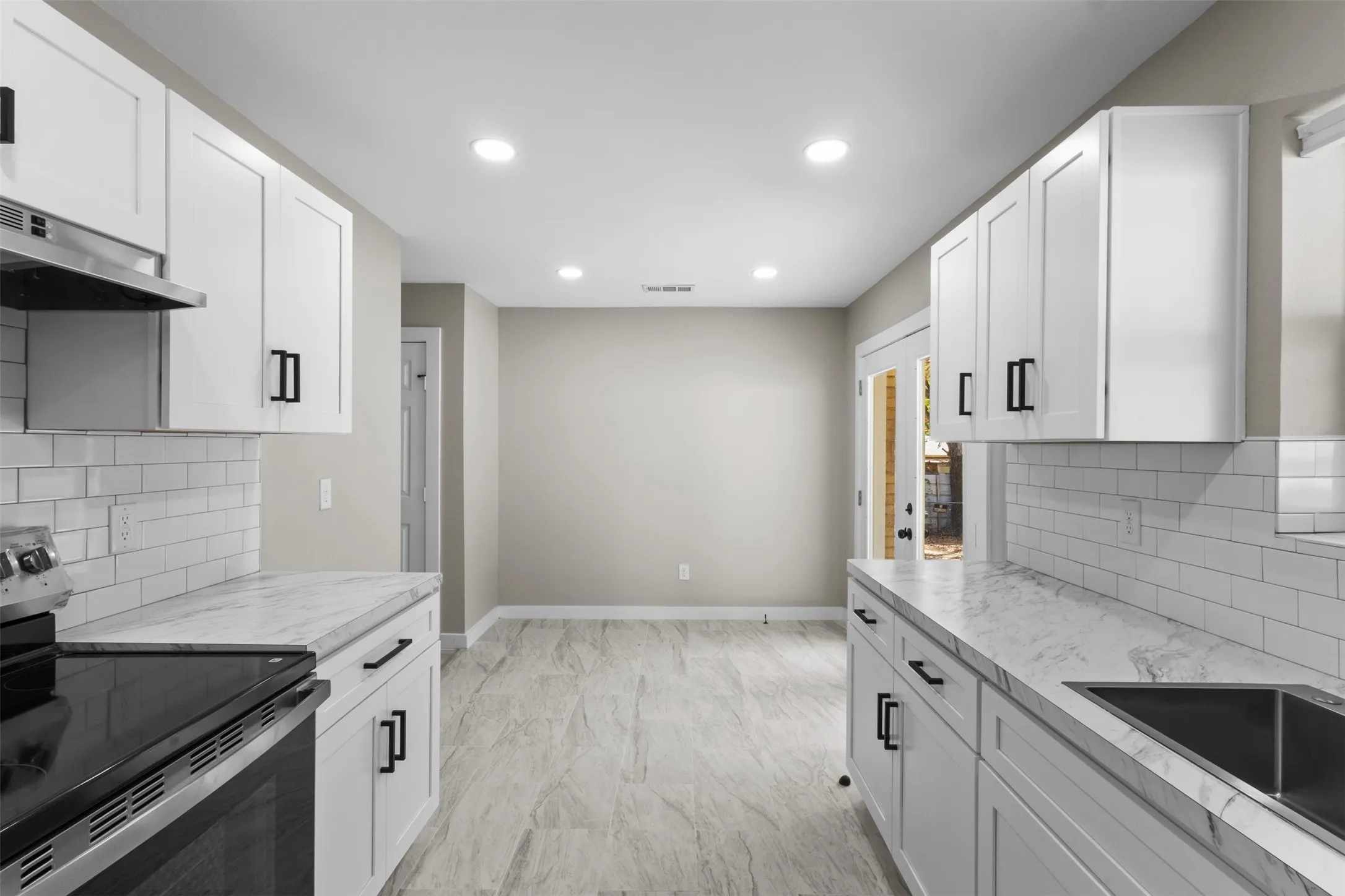 White shaker cabinetry with black hardware, subway tile backsplash, light-toned countertop, stainless steel sink, and recessed lighting