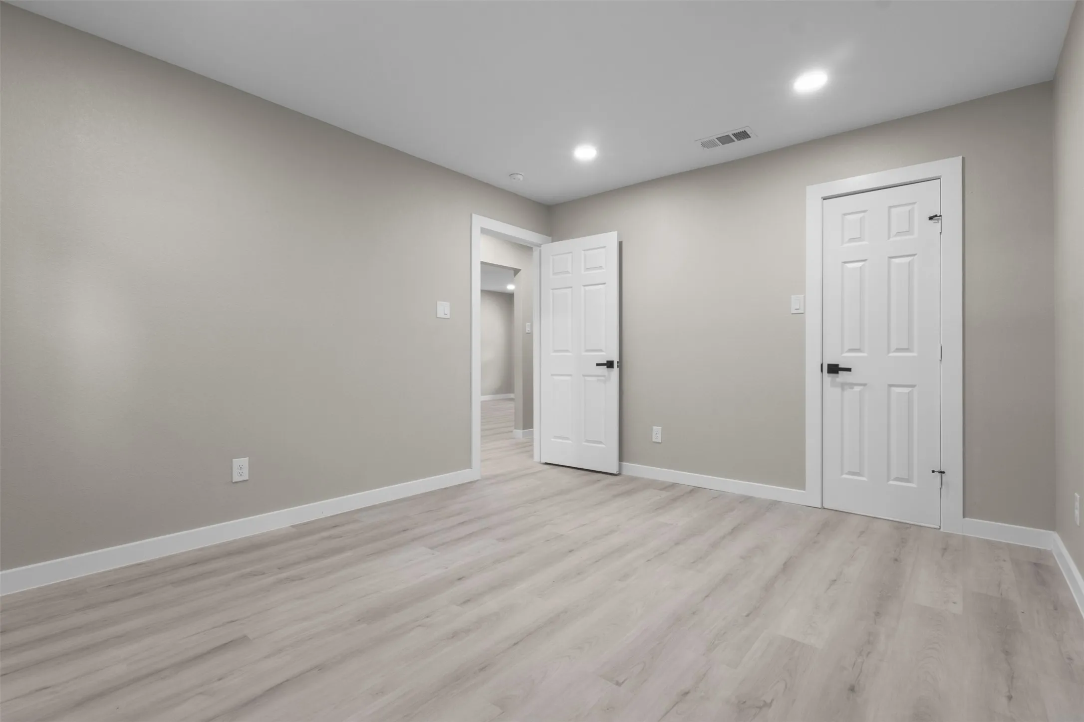 Pale gray wall finishes, wood-finish flooring, white trim, recessed lighting, and white paneled doors with black hardware