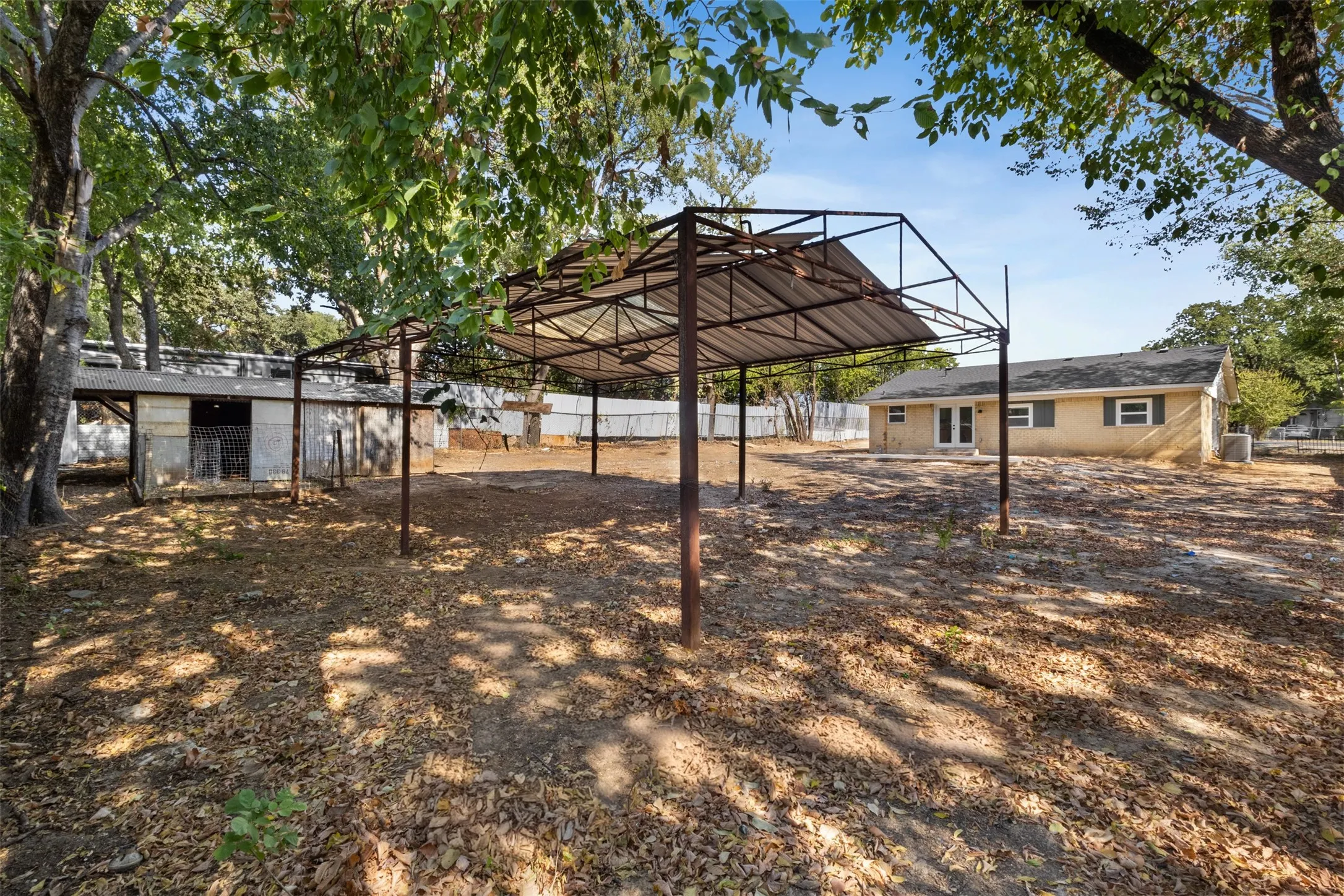 Expansive outdoor space featuring a covered metal structure, additional outbuilding, and mature trees