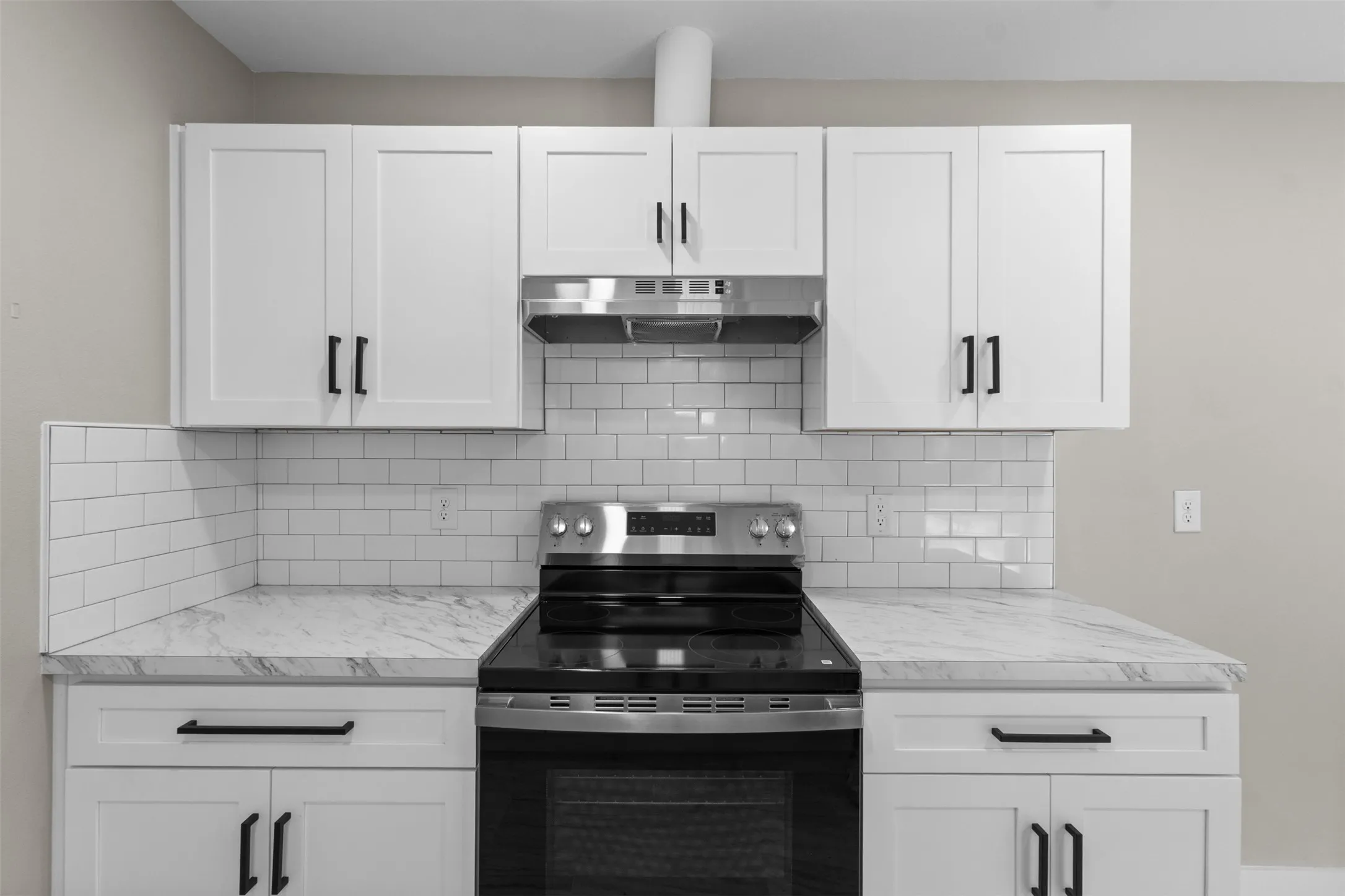 White shaker-style cabinetry, subway tile backsplash, stainless steel range hood, electric range, and patterned countertops