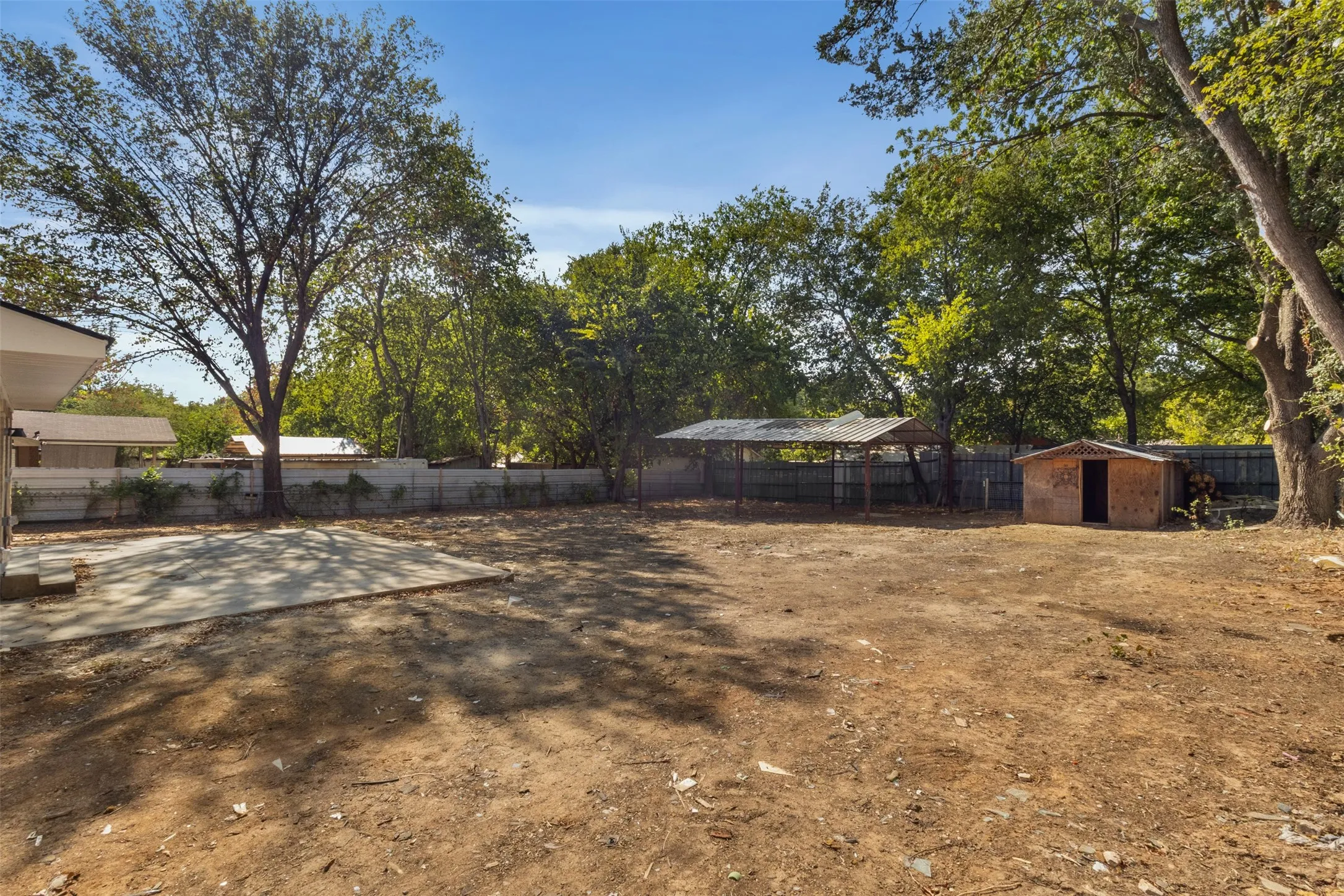 Expansive outdoor space featuring a concrete patio, mature trees, a detached storage shed, and a covered structure