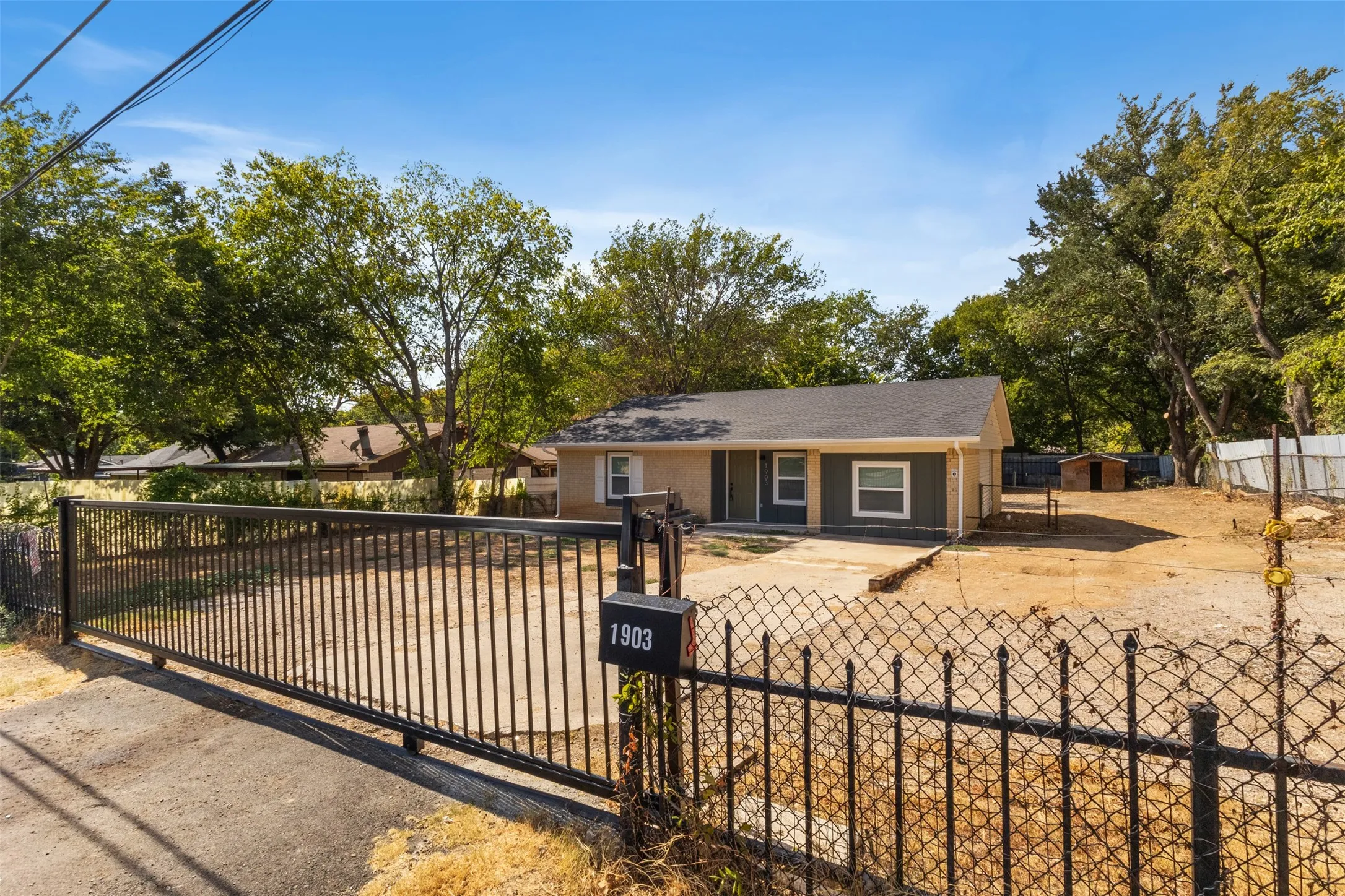 Charming single-story residence with a tan exterior and dark trim, situated on an expansive lot with mature shade trees