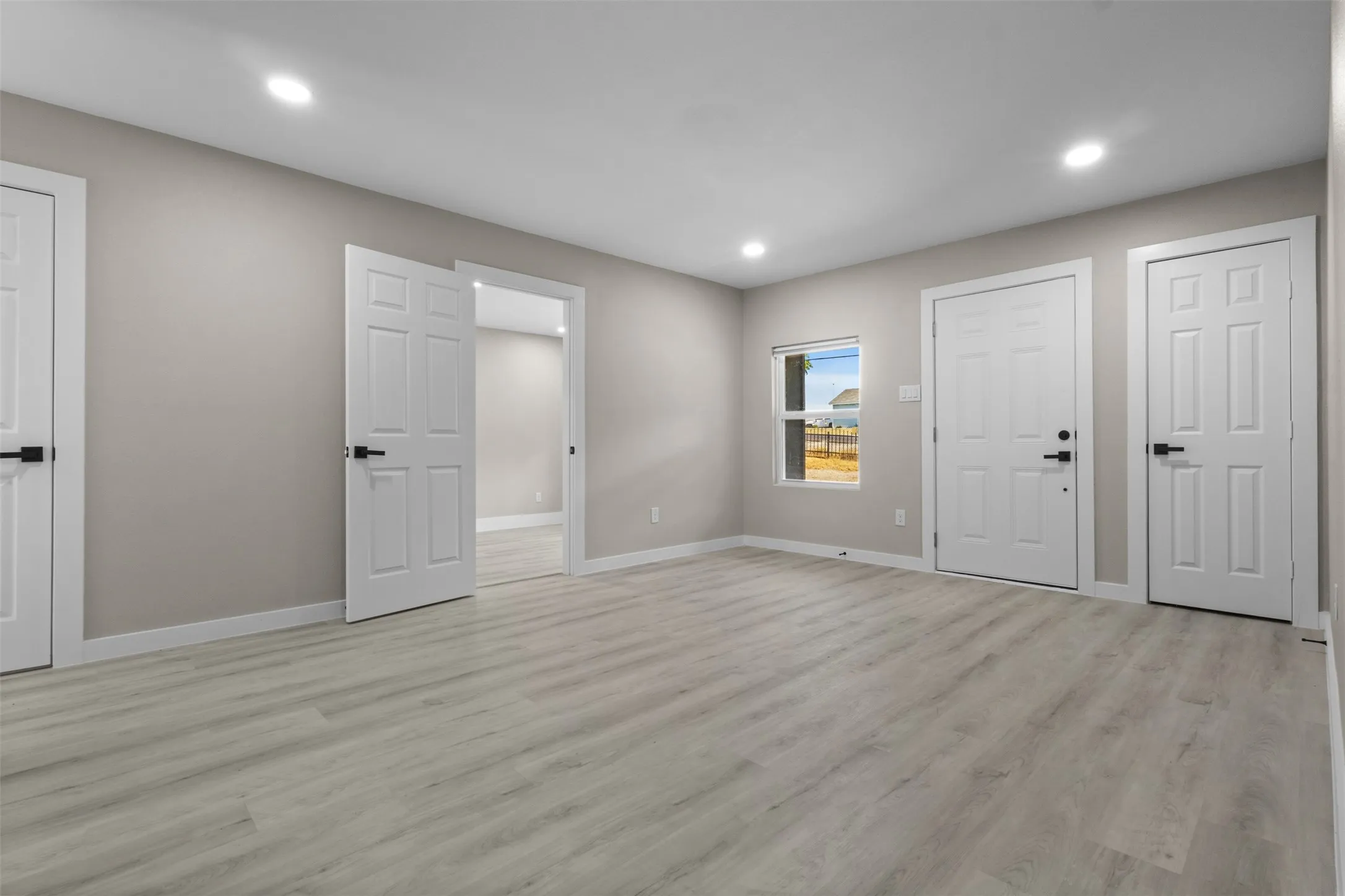 Recessed lighting, wood-finish flooring, light neutral wall paint, white trim, and a window with outdoor scenery